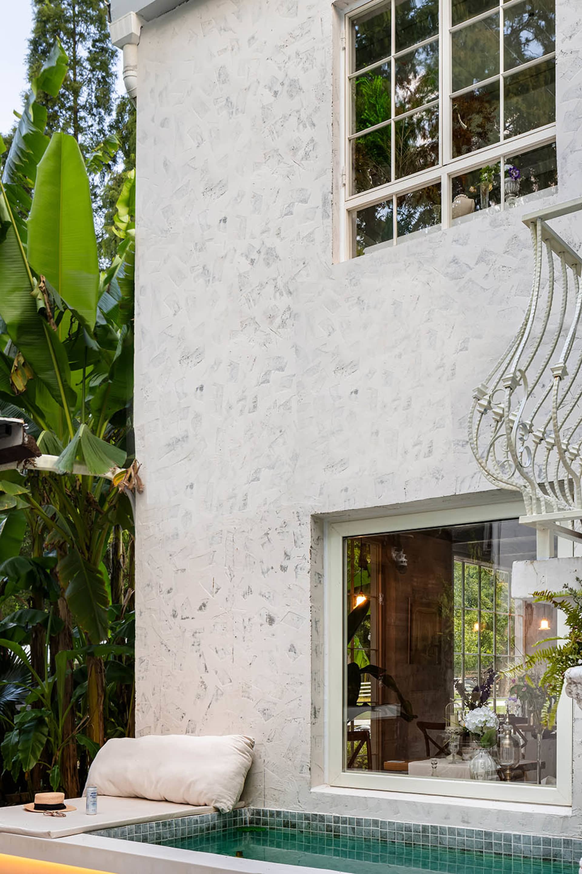 White stucco exterior of a minimalist residential outdoor space with a pool and greenery.