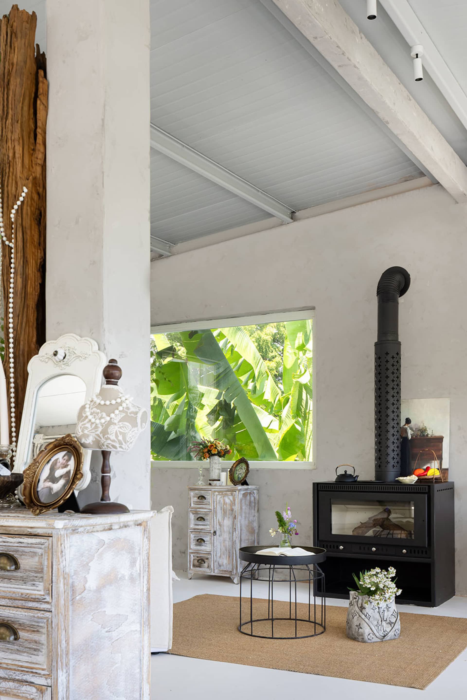 A spacious industrial living room with concrete walls and ceiling, large open windows, and a black stove with a natural wood