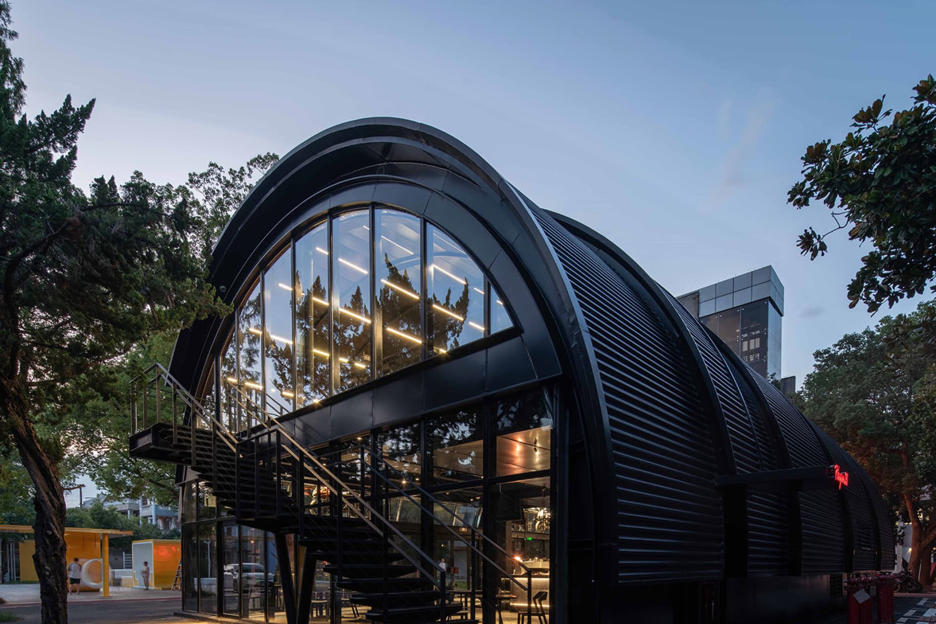A modern, black metal-clad building exterior with large glass windows and a curved roof.