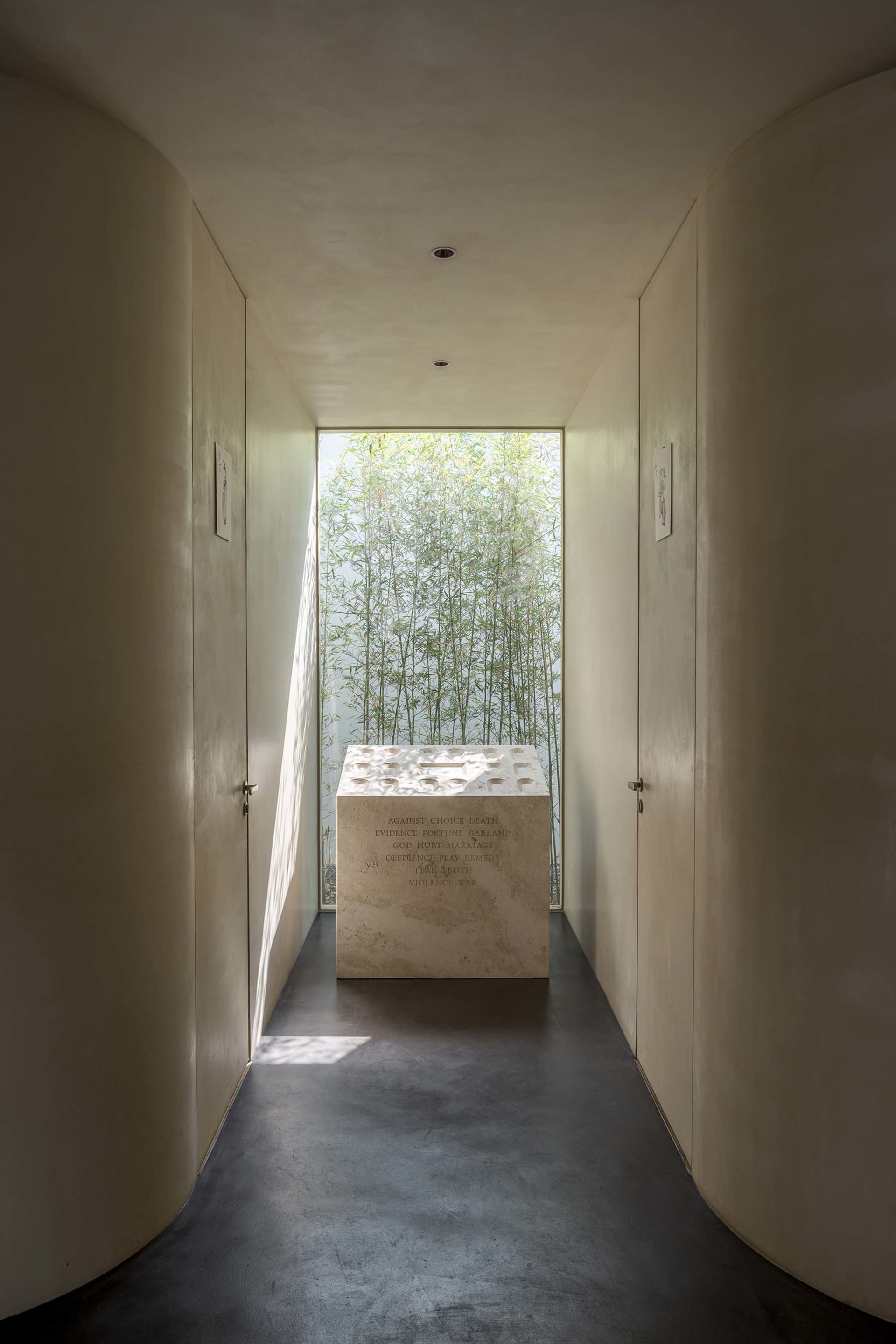 A modern, minimalist corridor featuring a concrete floor and walls with a large window showcasing green bamboo plants.