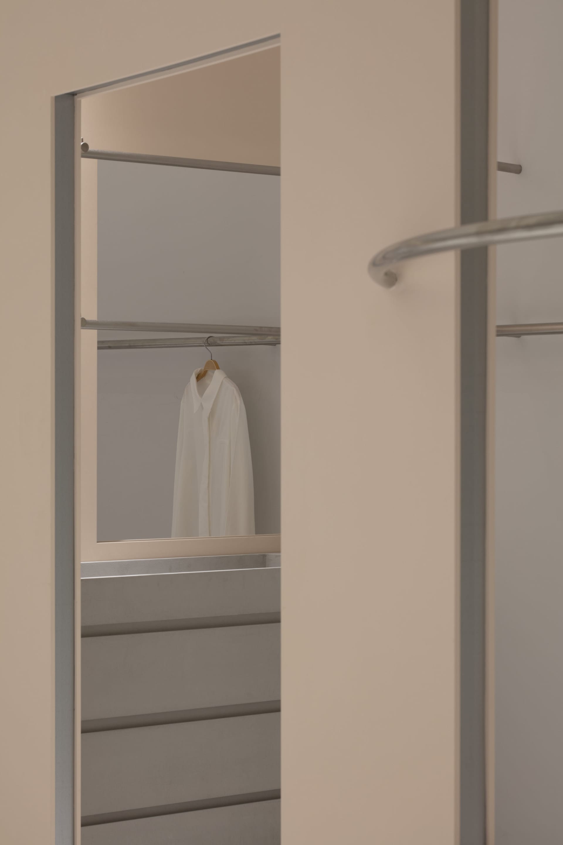 Modern minimalist closet with metallic clothing rack and white shirt hanging on hanger.