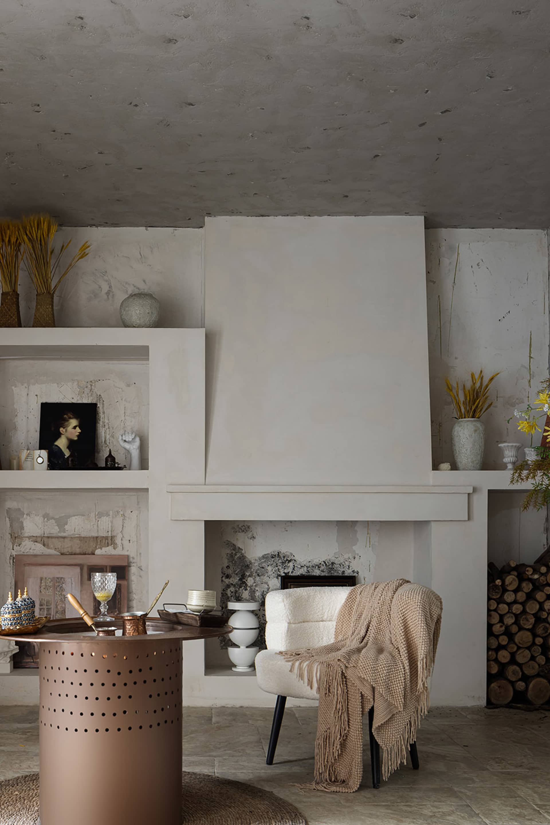 A modern minimalist living room with a concrete fireplace, wooden armchair with a beige throw blanket, and a circular metalli