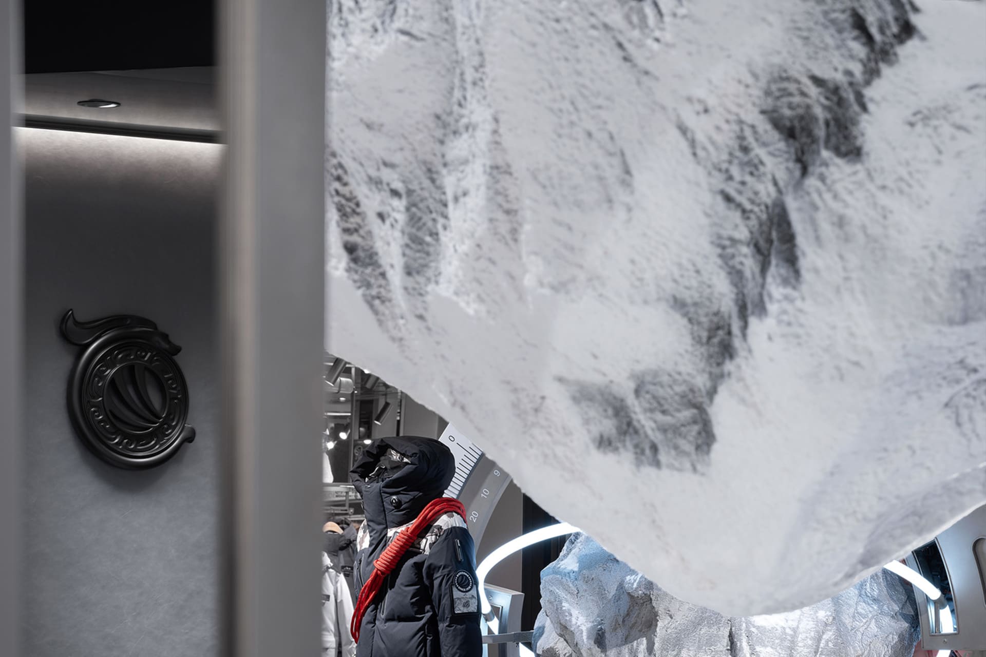 A modern interior shop display featuring a mannequin dressed in black clothing with a red scarf, under a large banner with a