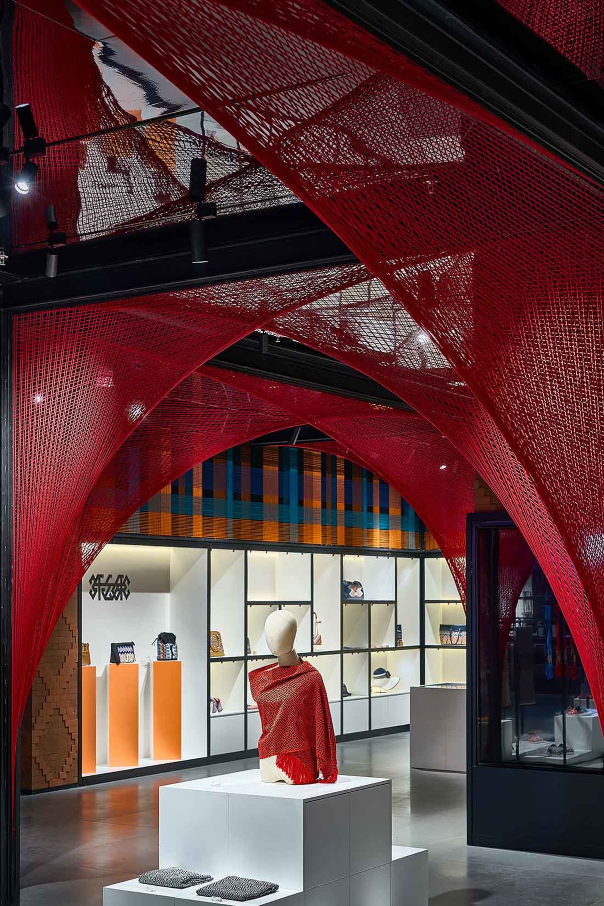 A retail store display featuring a mannequin draped in a red-netted garment, surrounded by a red-netted structure and various