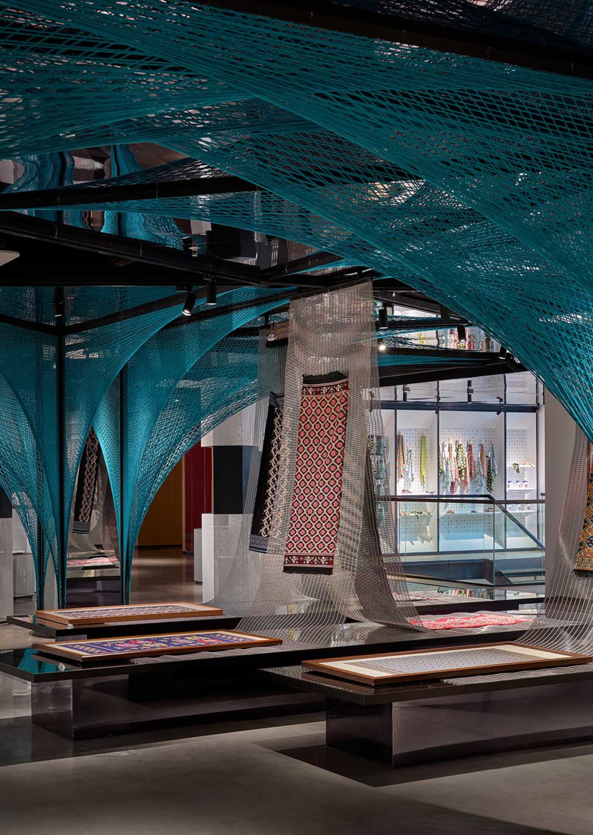 A modern retail store display featuring intricate blue netting and colorful textiles on tables and shelves.