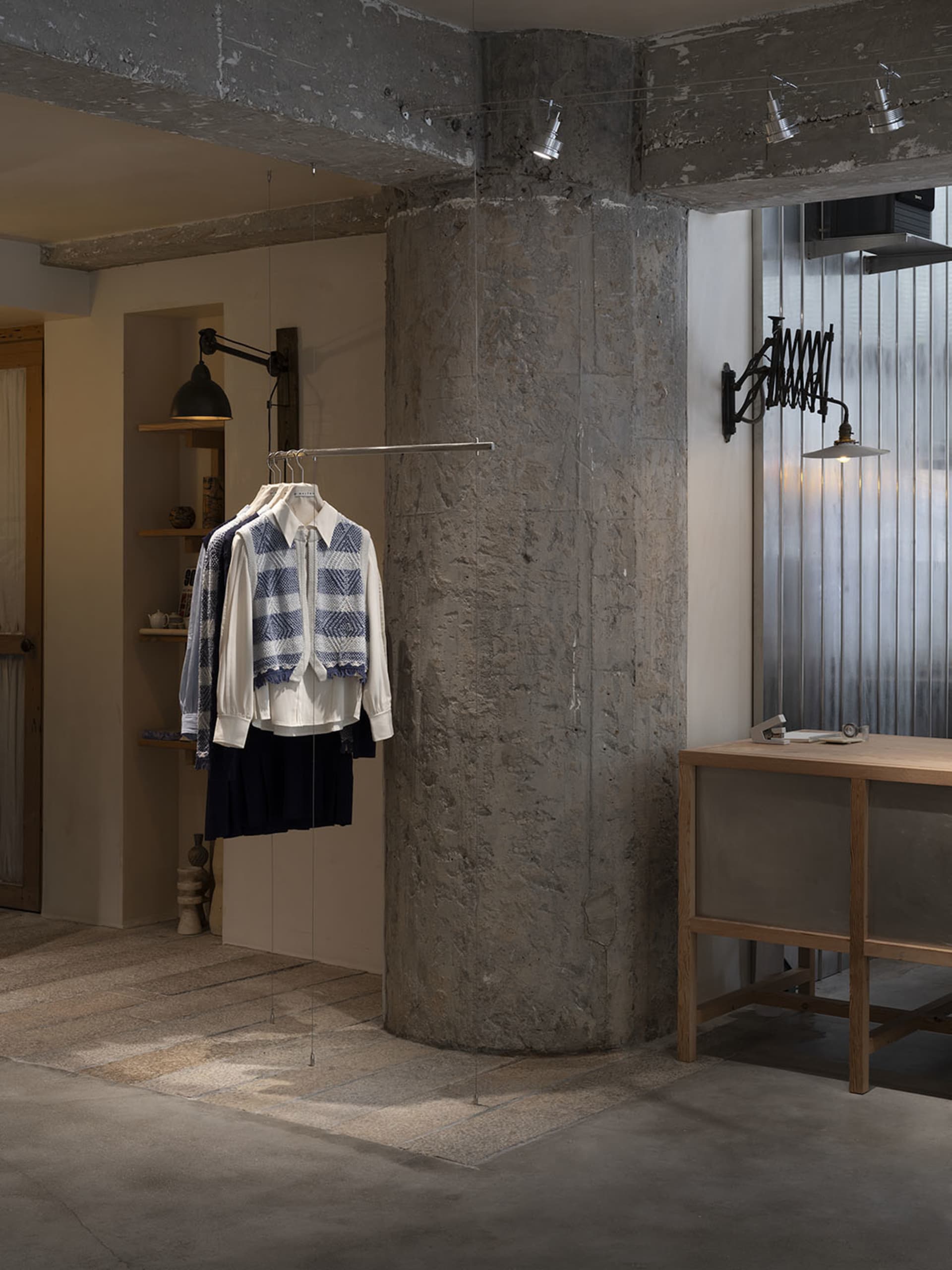 Retail space with concrete walls and metal accents, featuring modern clothing racks and a wooden table.