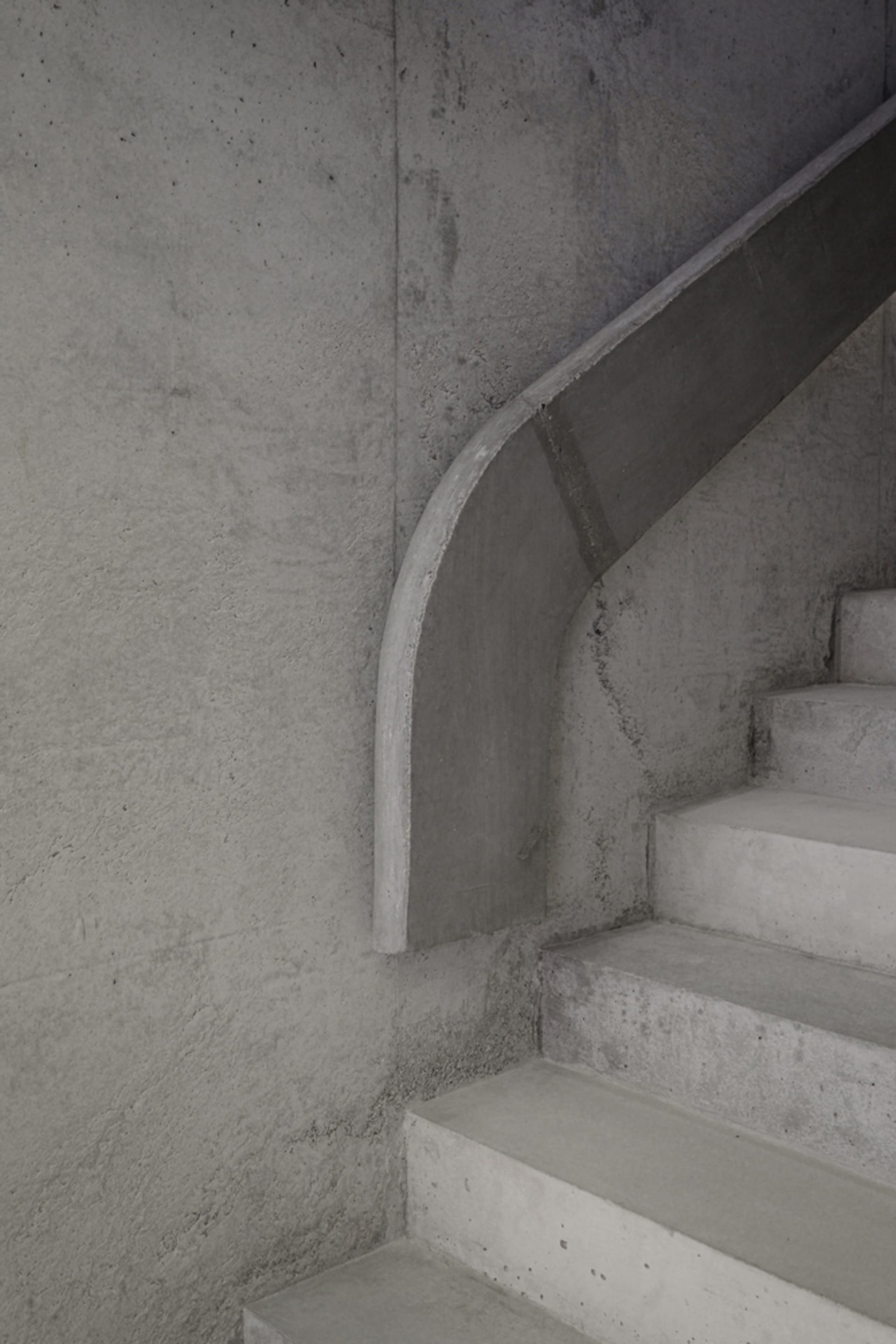 A modern, minimalist concrete staircase with smooth, curved risers against a textured concrete wall.