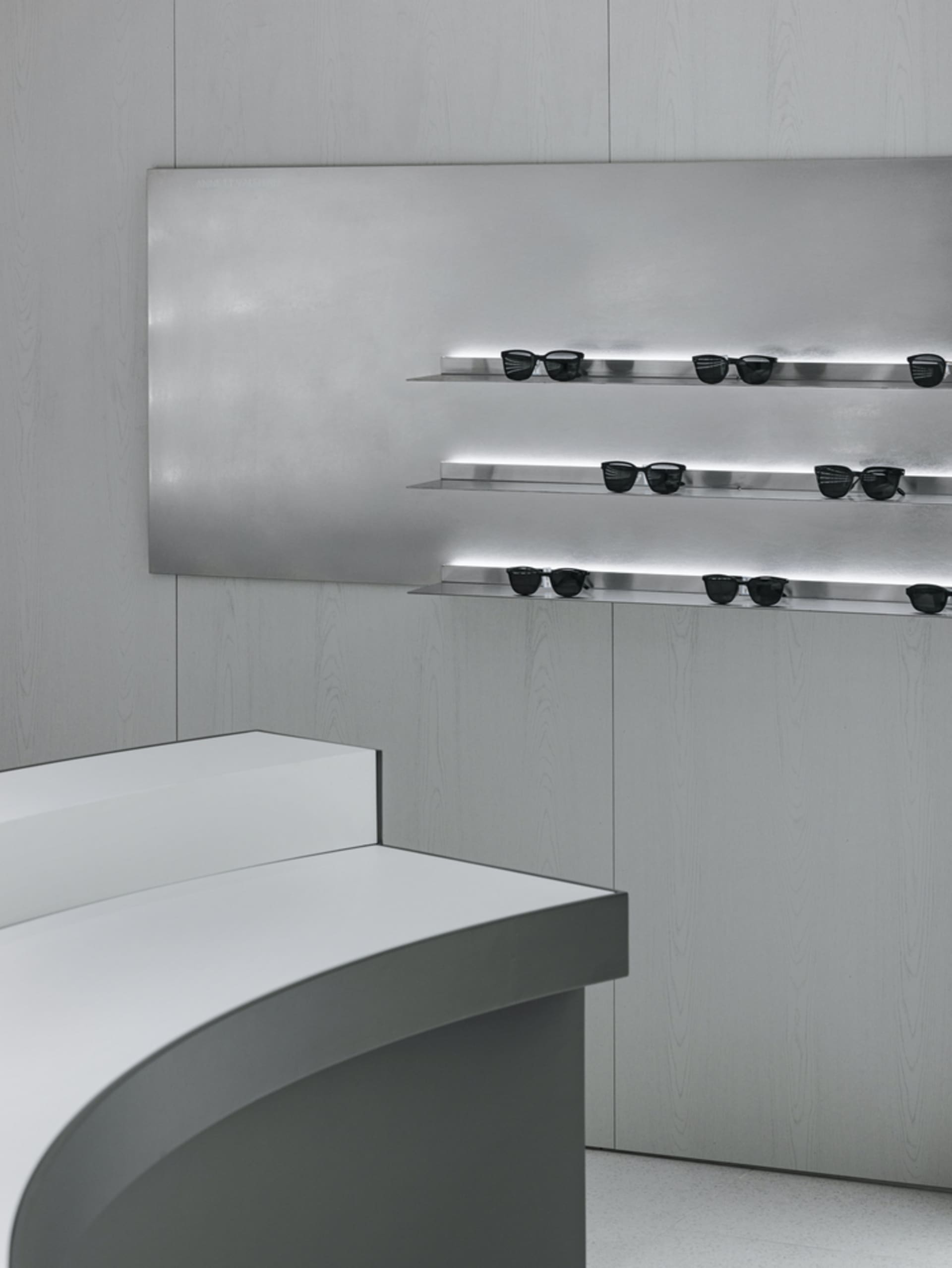 Minimalist glass counter with black metal shelves featuring black sunglasses in a retail storefront.