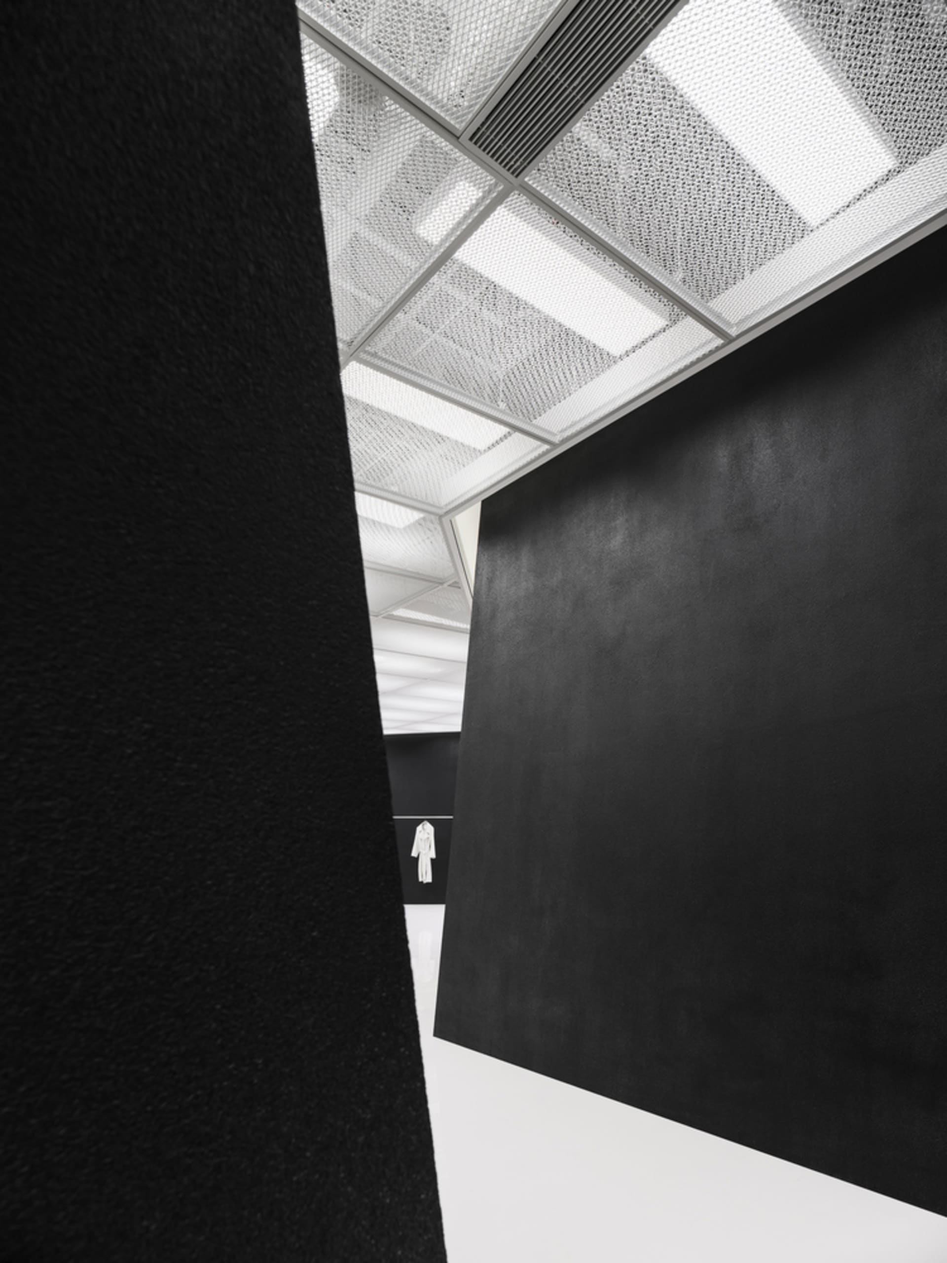 A minimalist interior space featuring black and white elements with a textured ceiling and a large, dark wall.