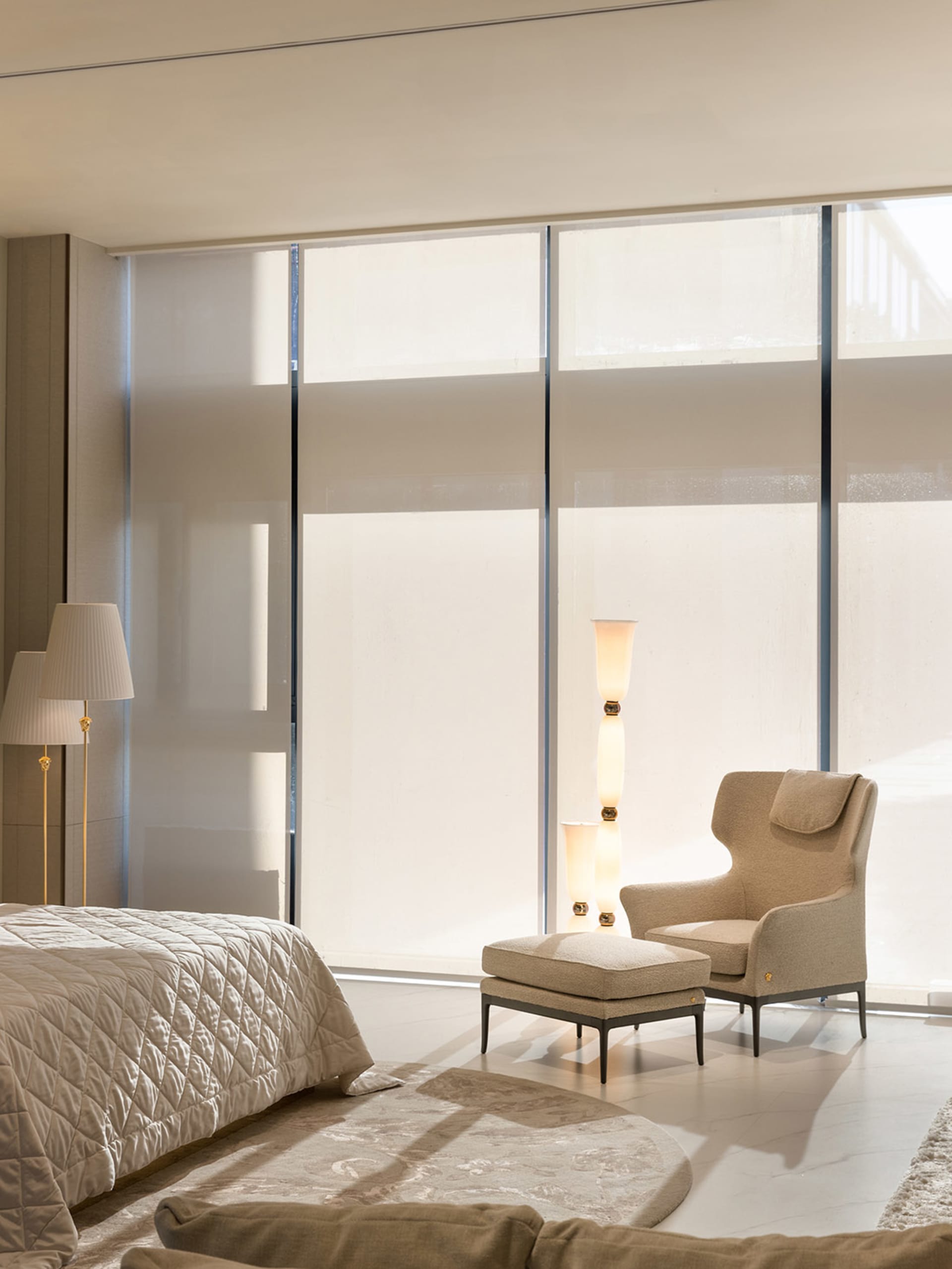 A serene bedroom with a neutral color palette, featuring a bed, armchair, and floor lamp.