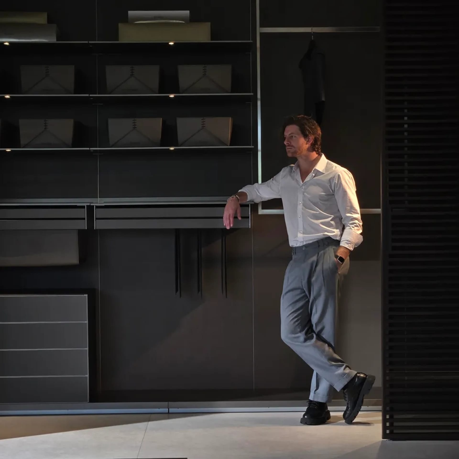 A man in a white shirt is leaning against metal shelves in a modern closet.