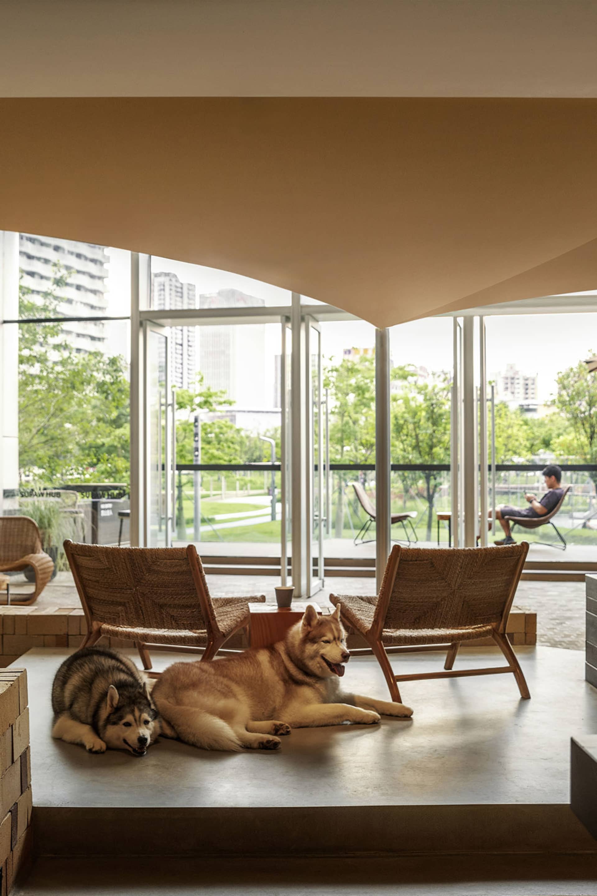 A cozy modern indoor living space featuring wooden furniture, concrete flooring, and a large glass window with outdoor views