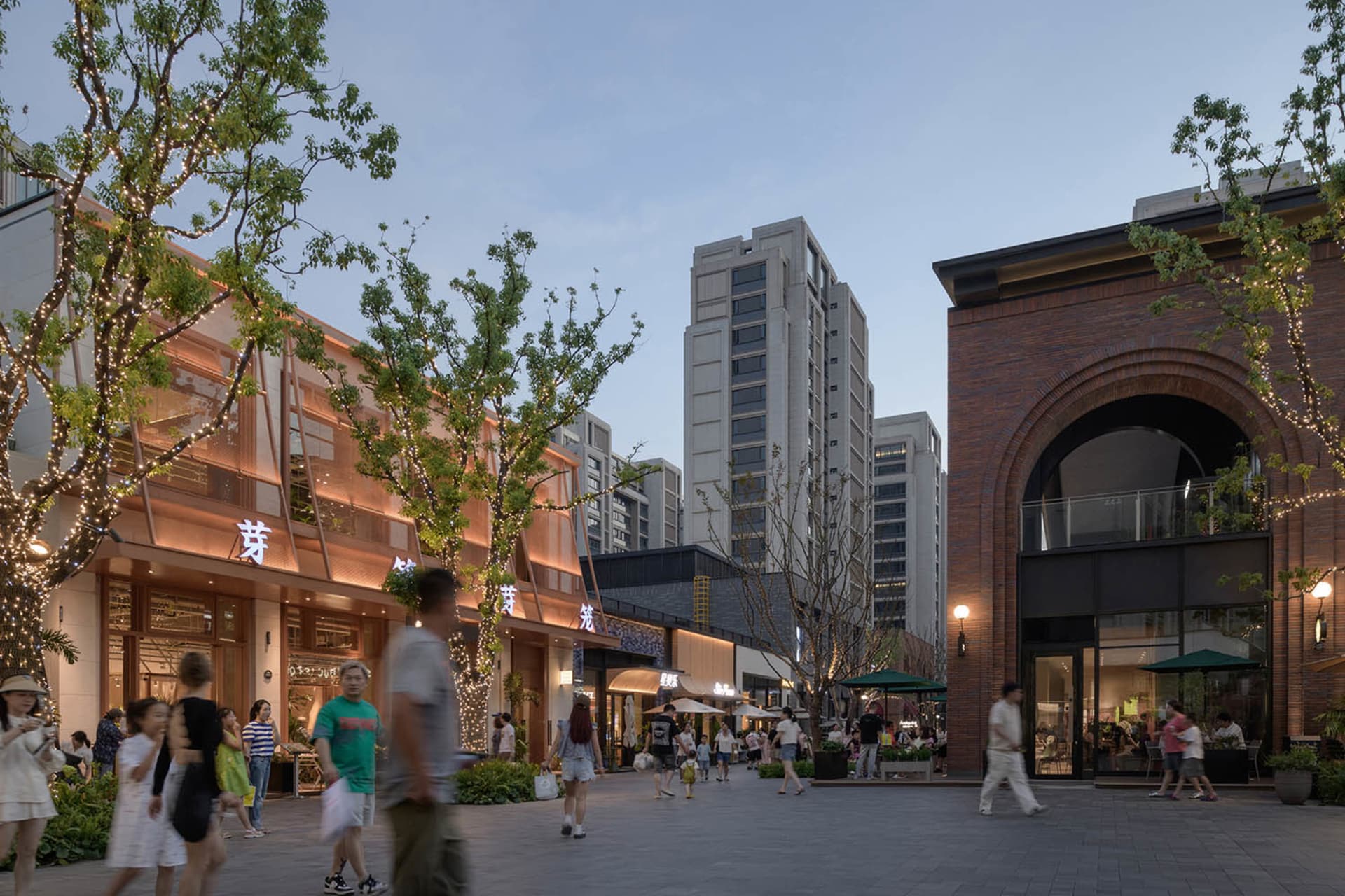 A bustling commercial mall with modern architecture featuring brick, concrete, glass, and lighting.