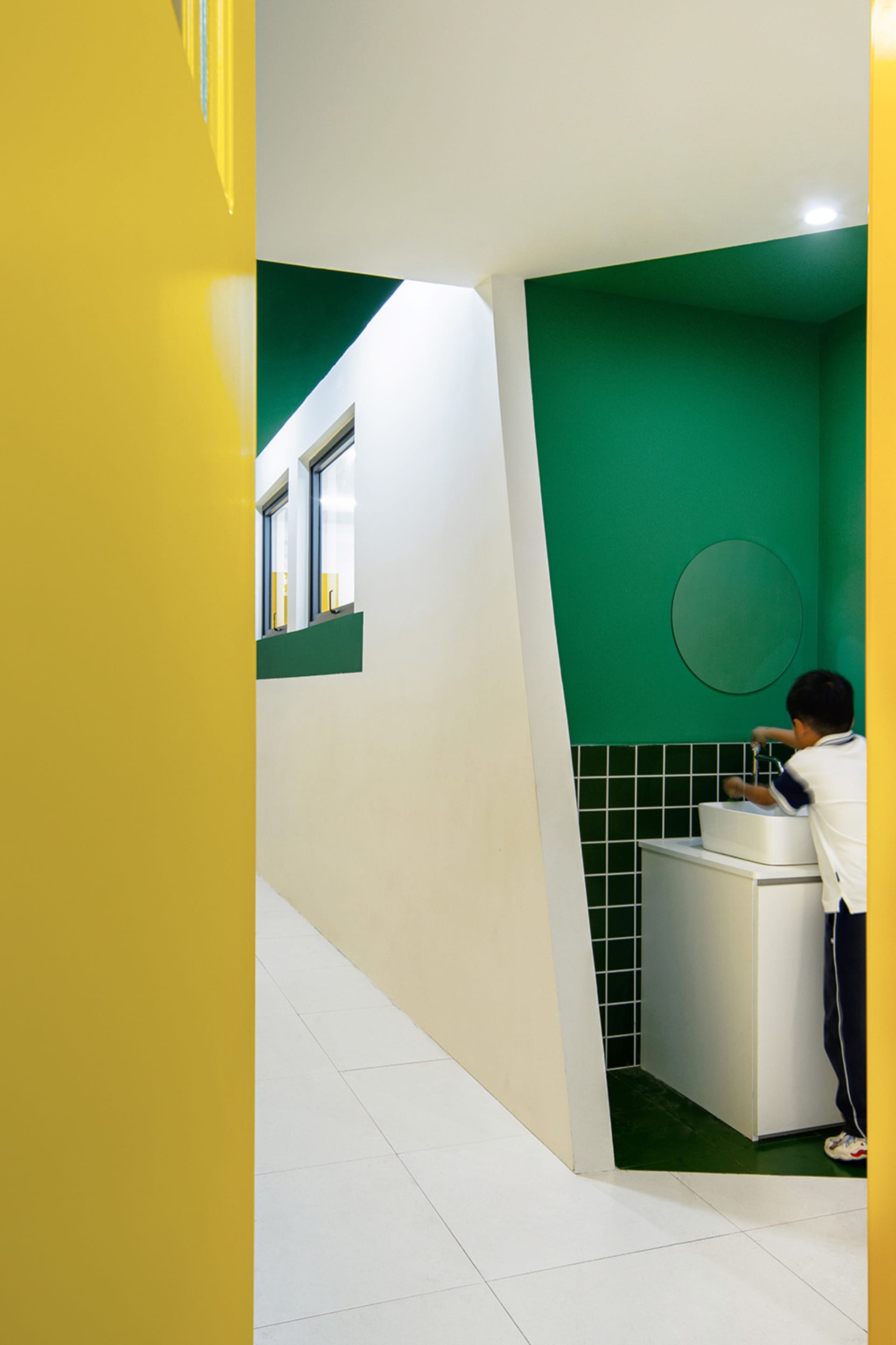 A modern public toilet interior with green and white colors, ceramic tiles, and a sink.