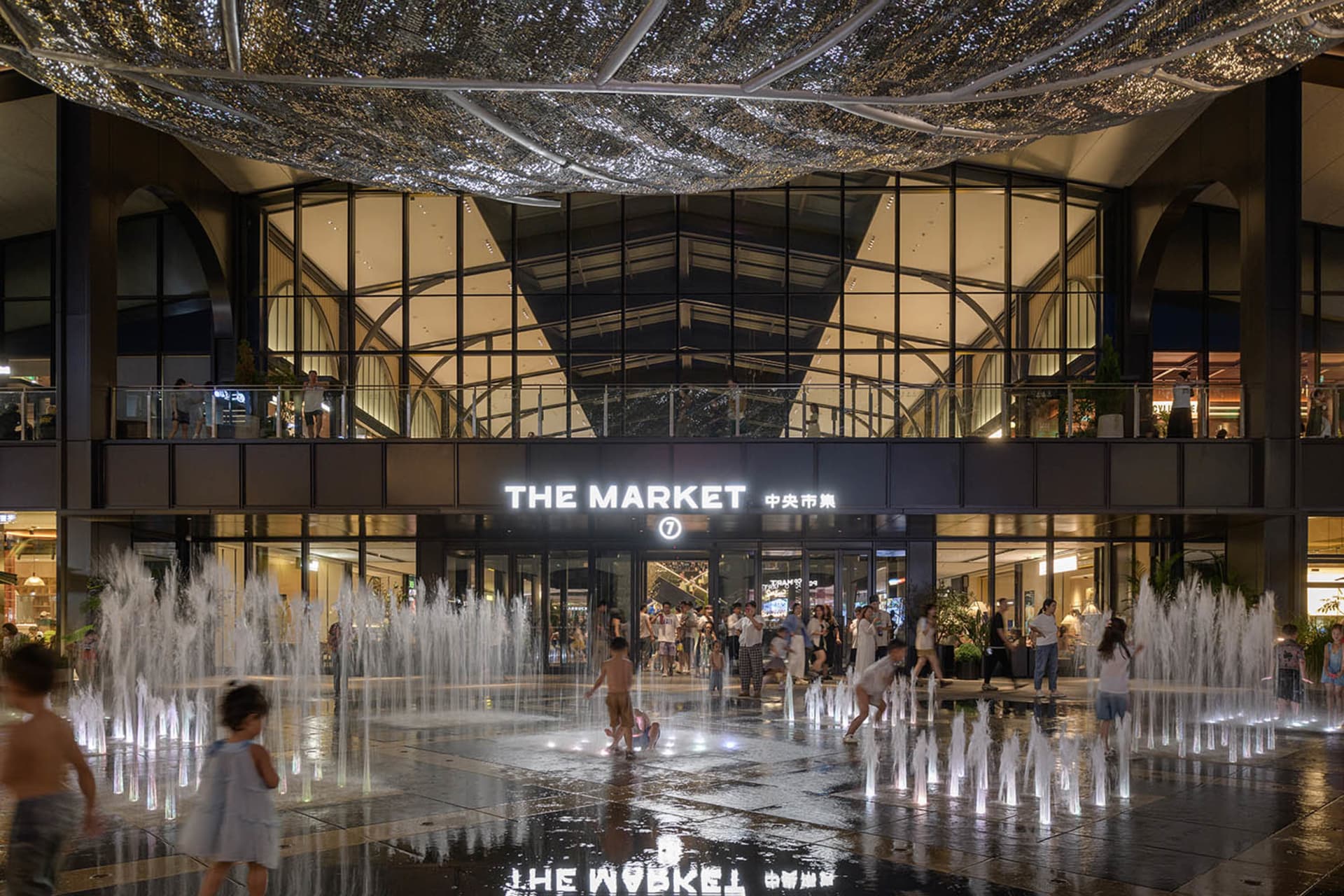 Children play in a water fountain area within a shopping center.