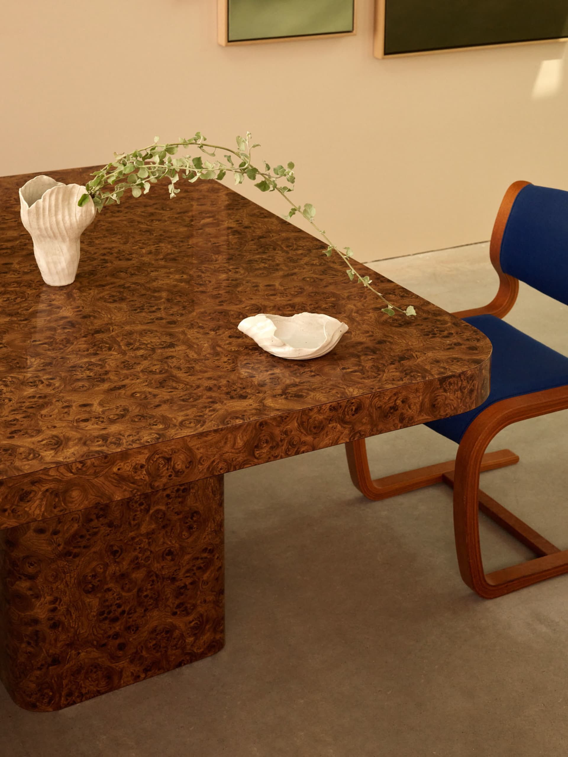 A modern work space featuring a burlwood table with a white ceramic vase and a white ceramic bowl with leaves.