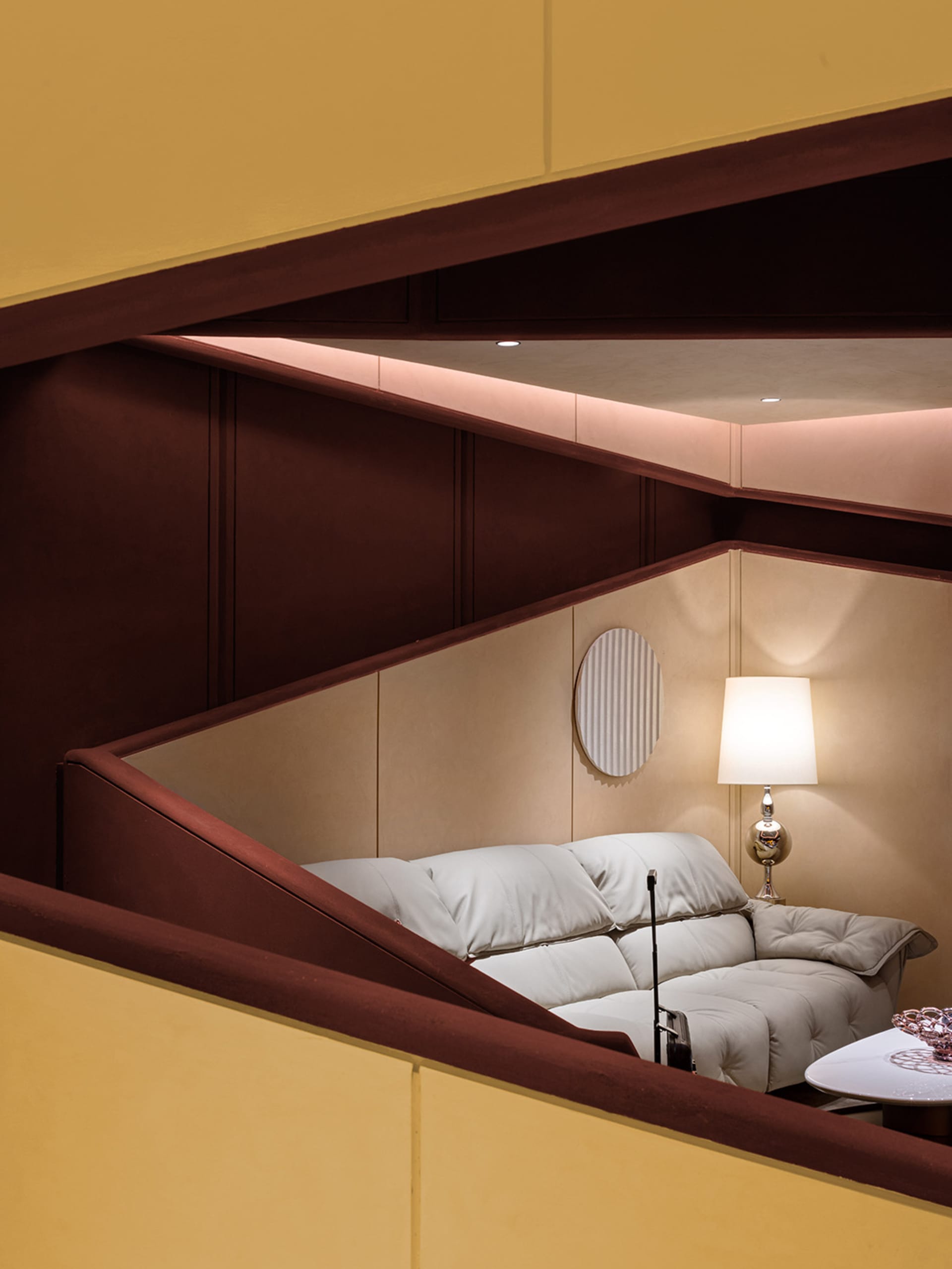 A cozy living room with a comfortable off-white sofa, a table lamp, and a circular patterned wall decor, set against a warm, 