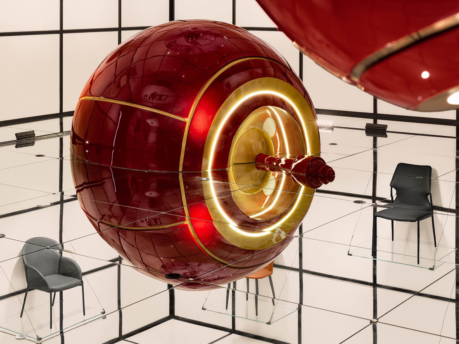 A red metallic sphere with a glowing gold interior, suspended in a modern installation setting.