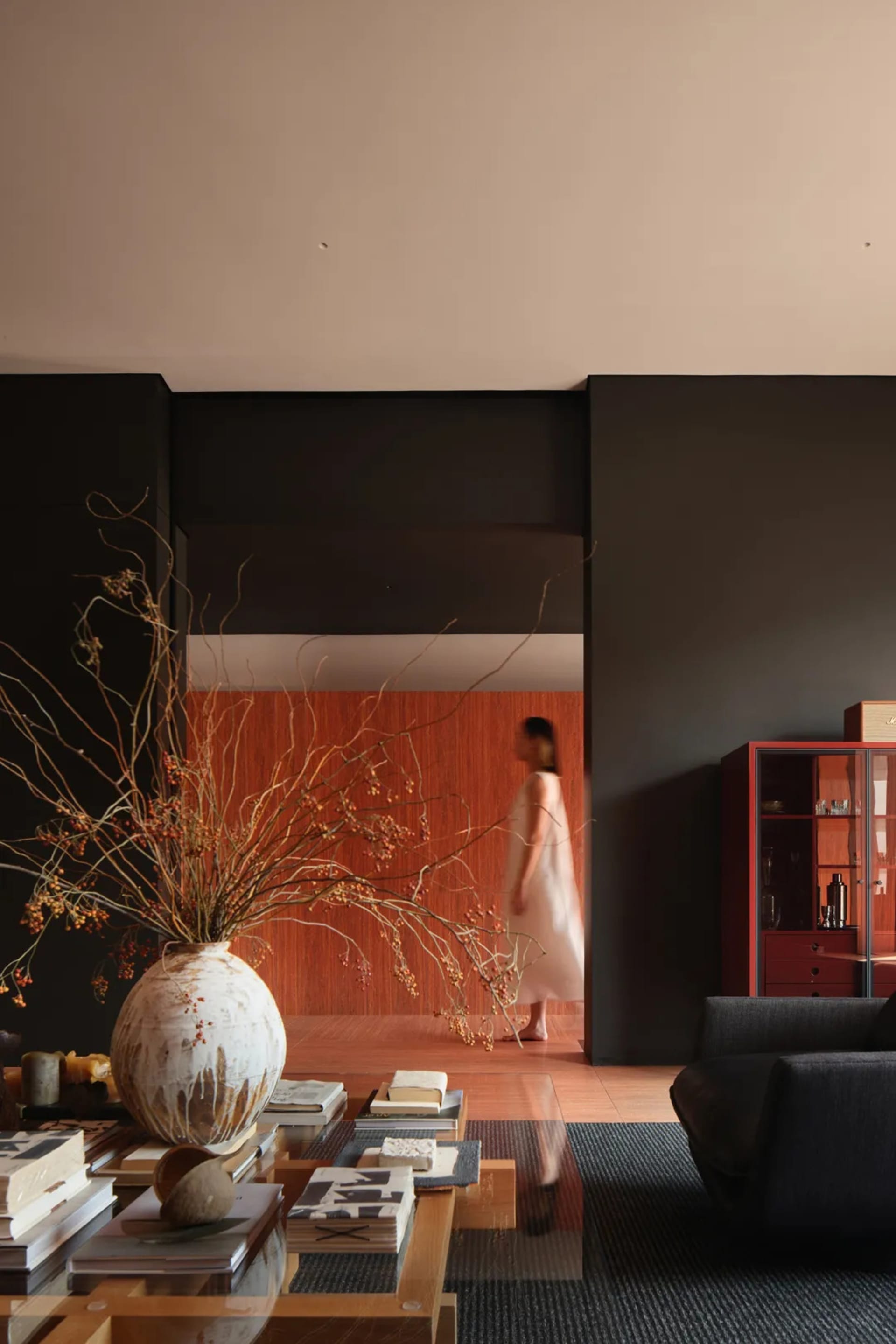 A modern interior living space featuring a large vase with dried flowers, a coffee table with books and decor items, and a pe