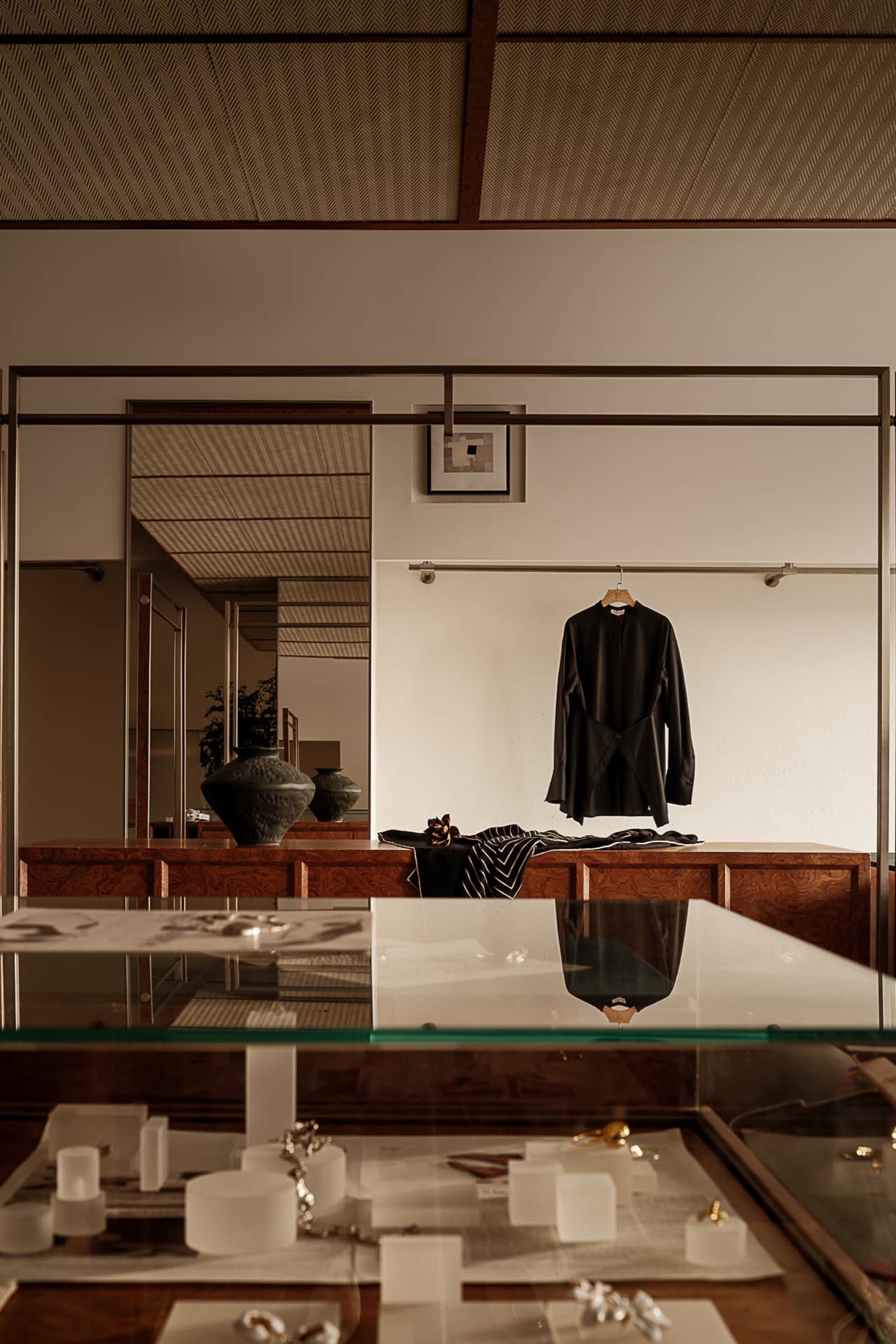 A stylish clothing shop display featuring a glass table with jewelry and clothing, and a wooden cabinet with a black shirt ha