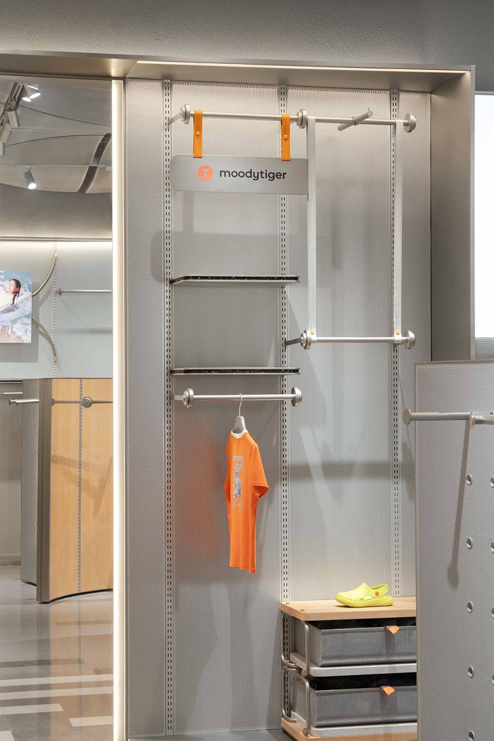 A clothing store display with metal rails and metal panels featuring a single orange shirt hanging on a rod.