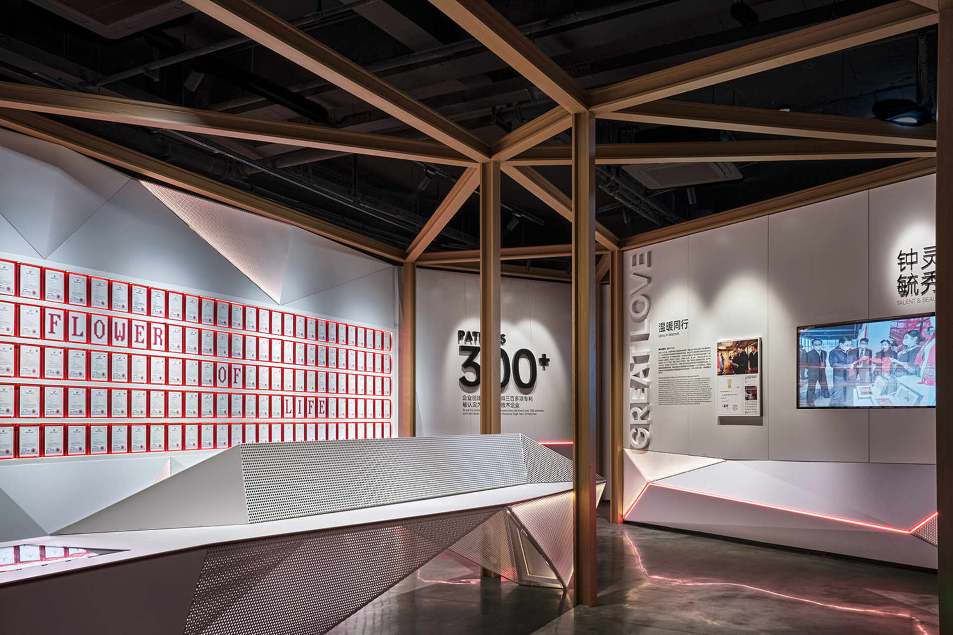 A modern exhibition space with metallic elements and certificates displayed on the wall, illuminated with red lighting.