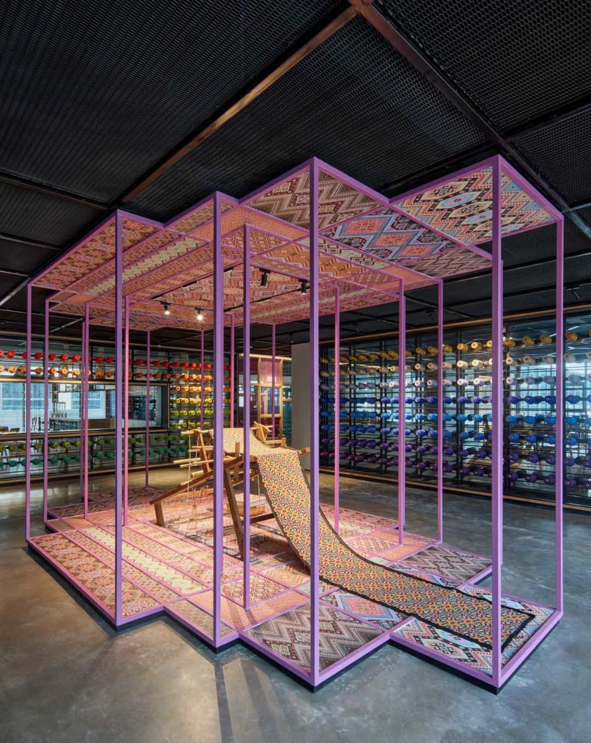 A colorful, patterned space with a textile weaving loom and a variety of yarn spools on display.