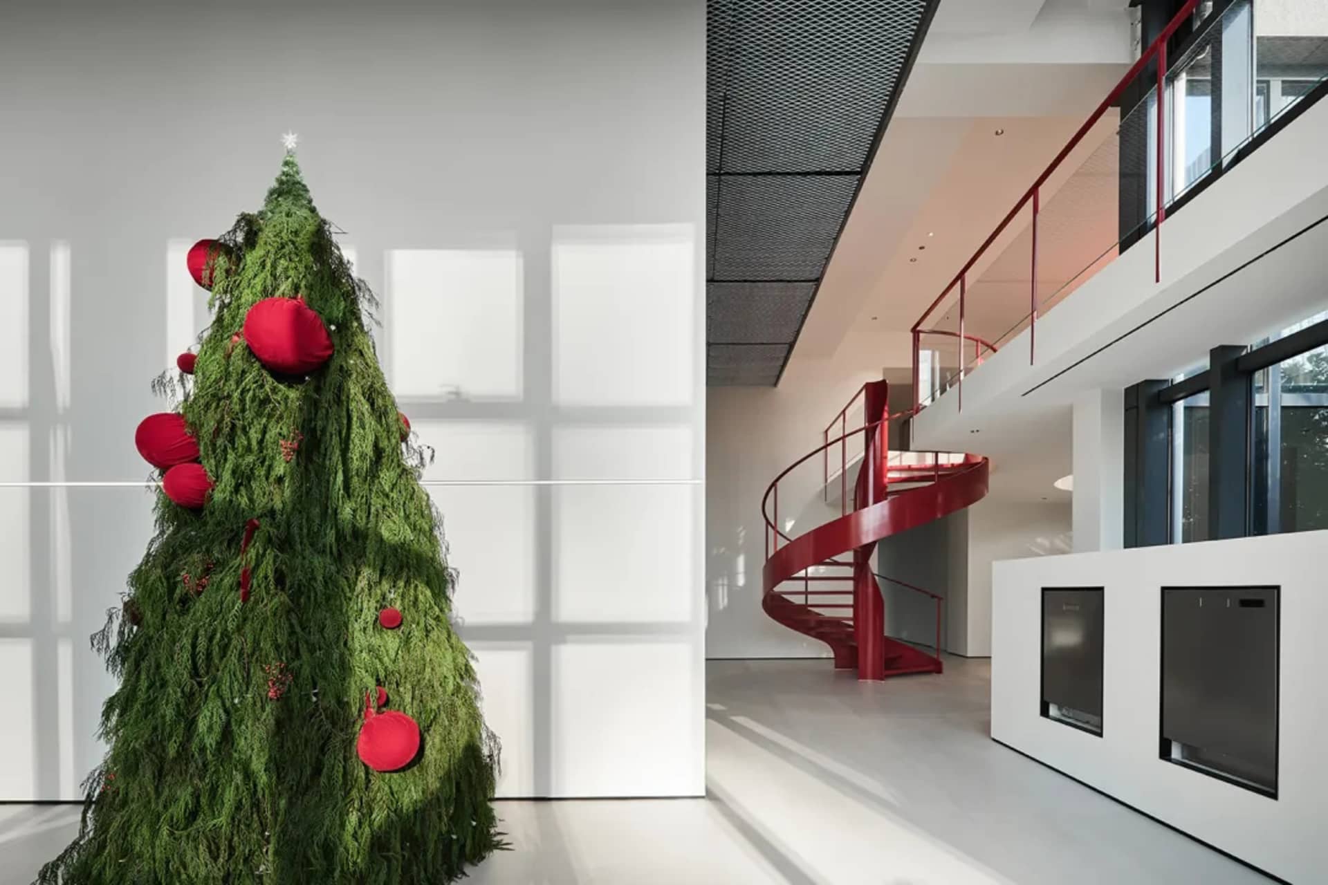 A large Christmas tree decorated with red baubles next to a white wall.