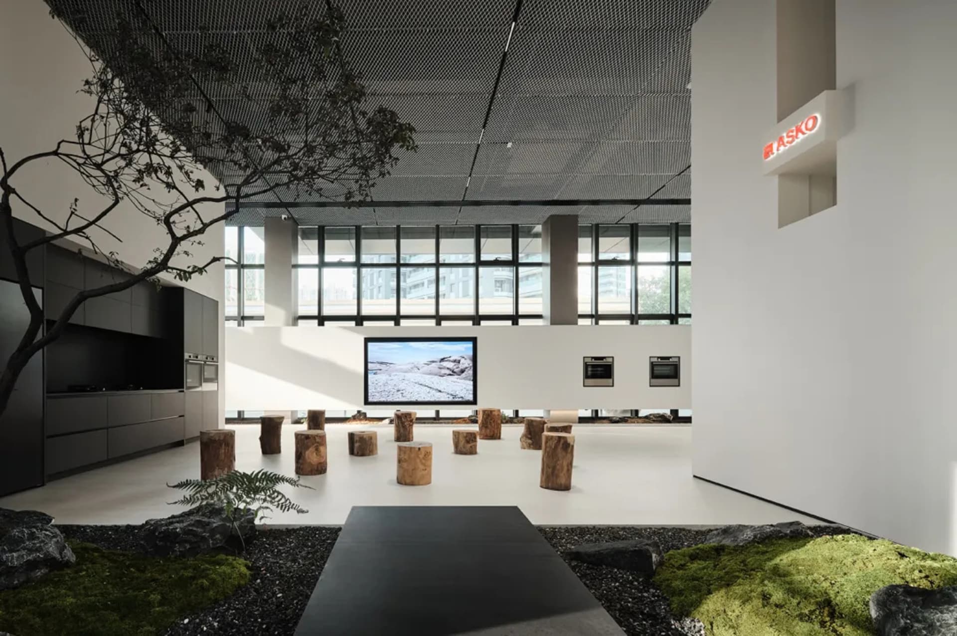 A modern kitchen exhibition room featuring wood stools and a large screen displaying a snowy landscape.