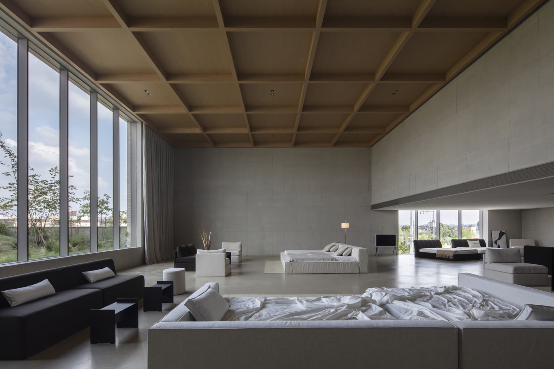 A minimalist living room with concrete walls and large windows, featuring a modern sofa and centered bed.