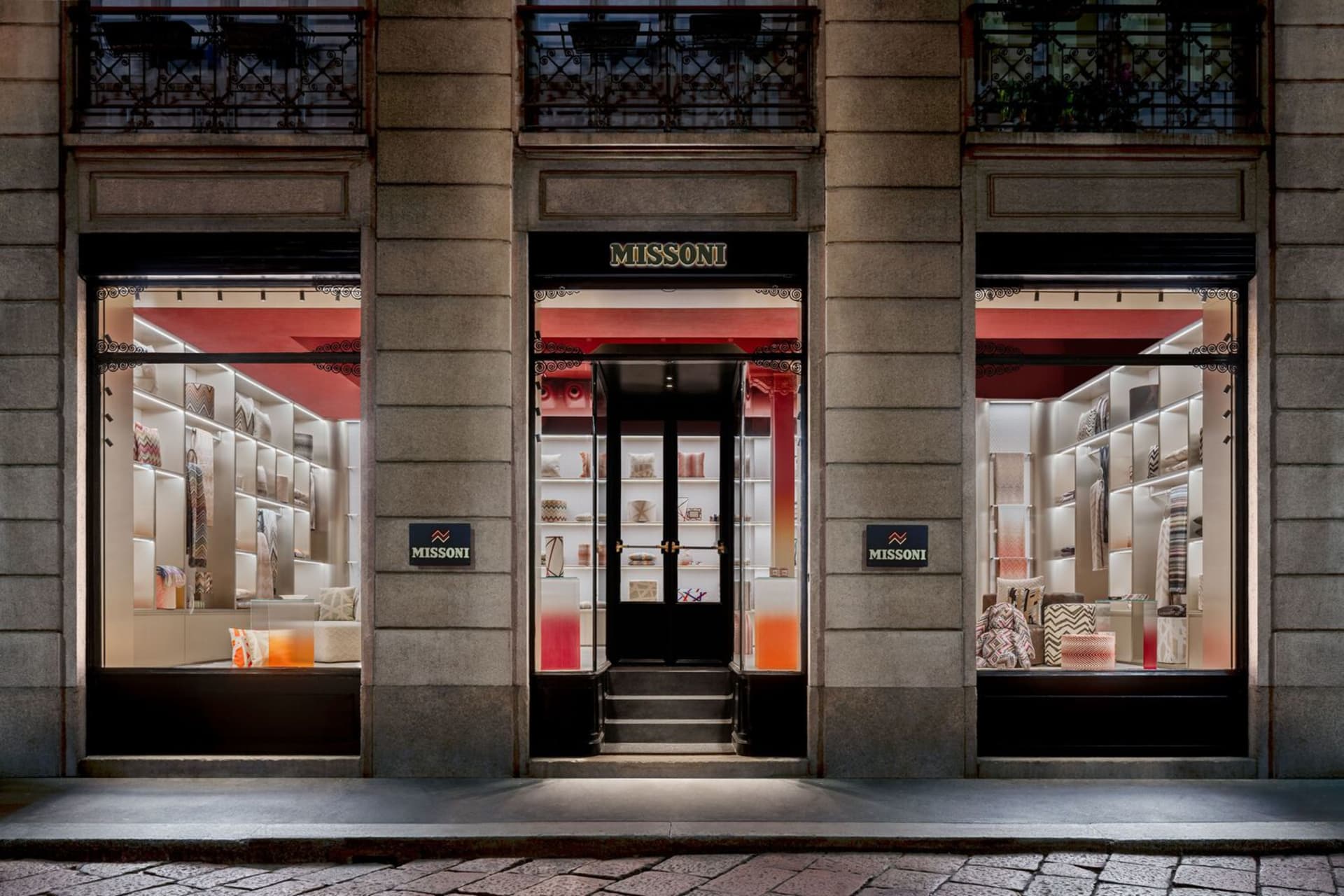 A modern storefront with glass windows displaying retail items, featuring a metal door and exterior wrought iron railing.