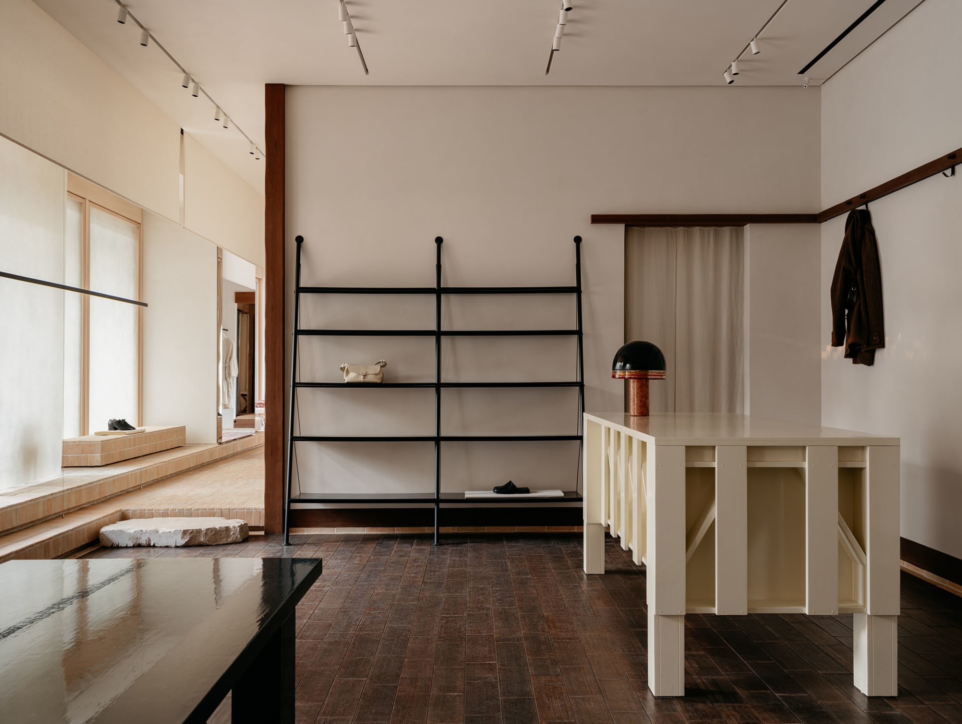 A modern retail space featuring black metal shelves, a white table, and a mix of materials including wood, fabric, and stone.
