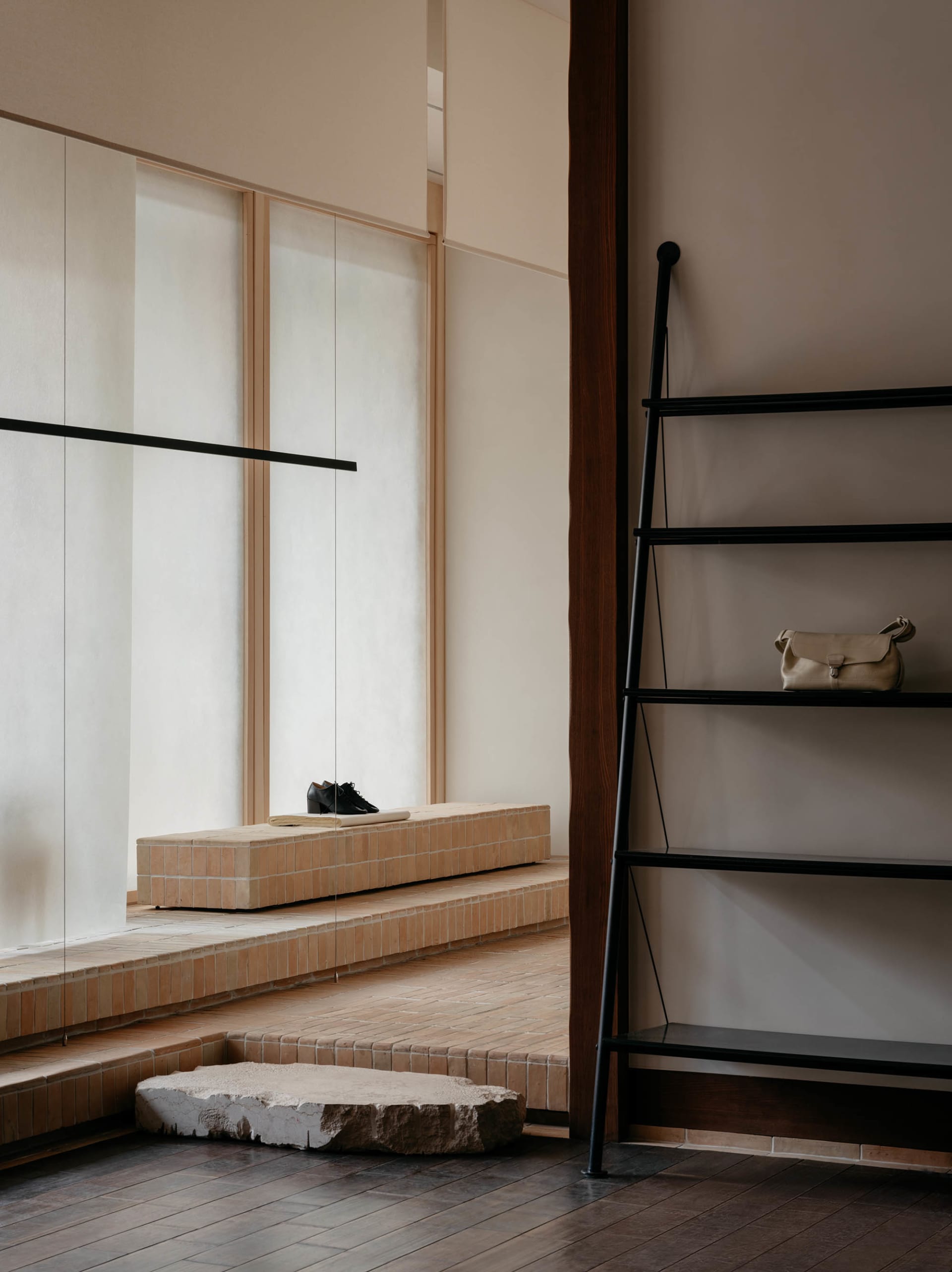 A minimalist shoe store interior with a brick counter and a black ladder with a leather bag.
