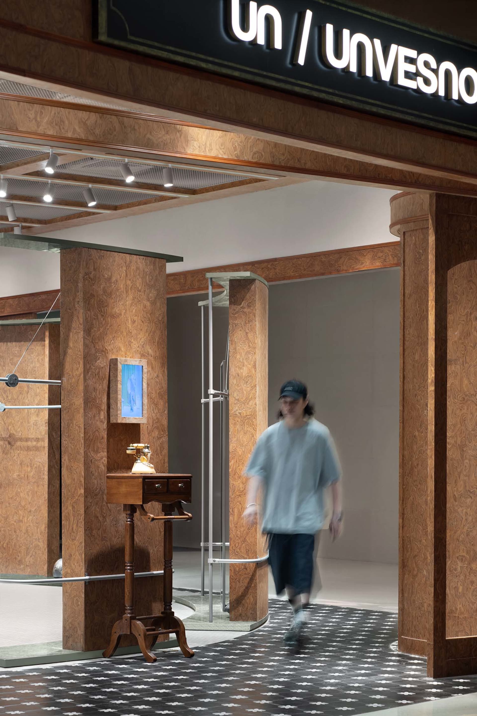 A storefront entry with wooden pillars and a patterned floor, featuring a vintage telephone and a mirror.