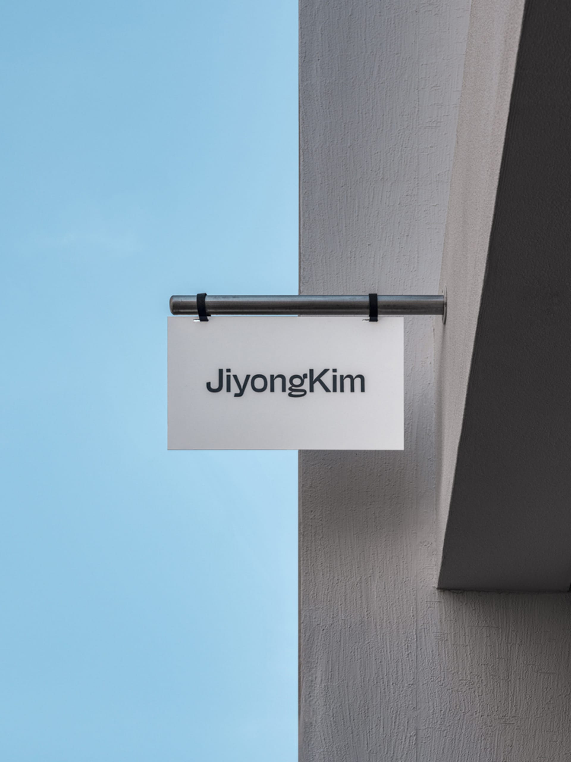 A minimalist signboard made of steel with the name 'Jiyong Kim' on it.