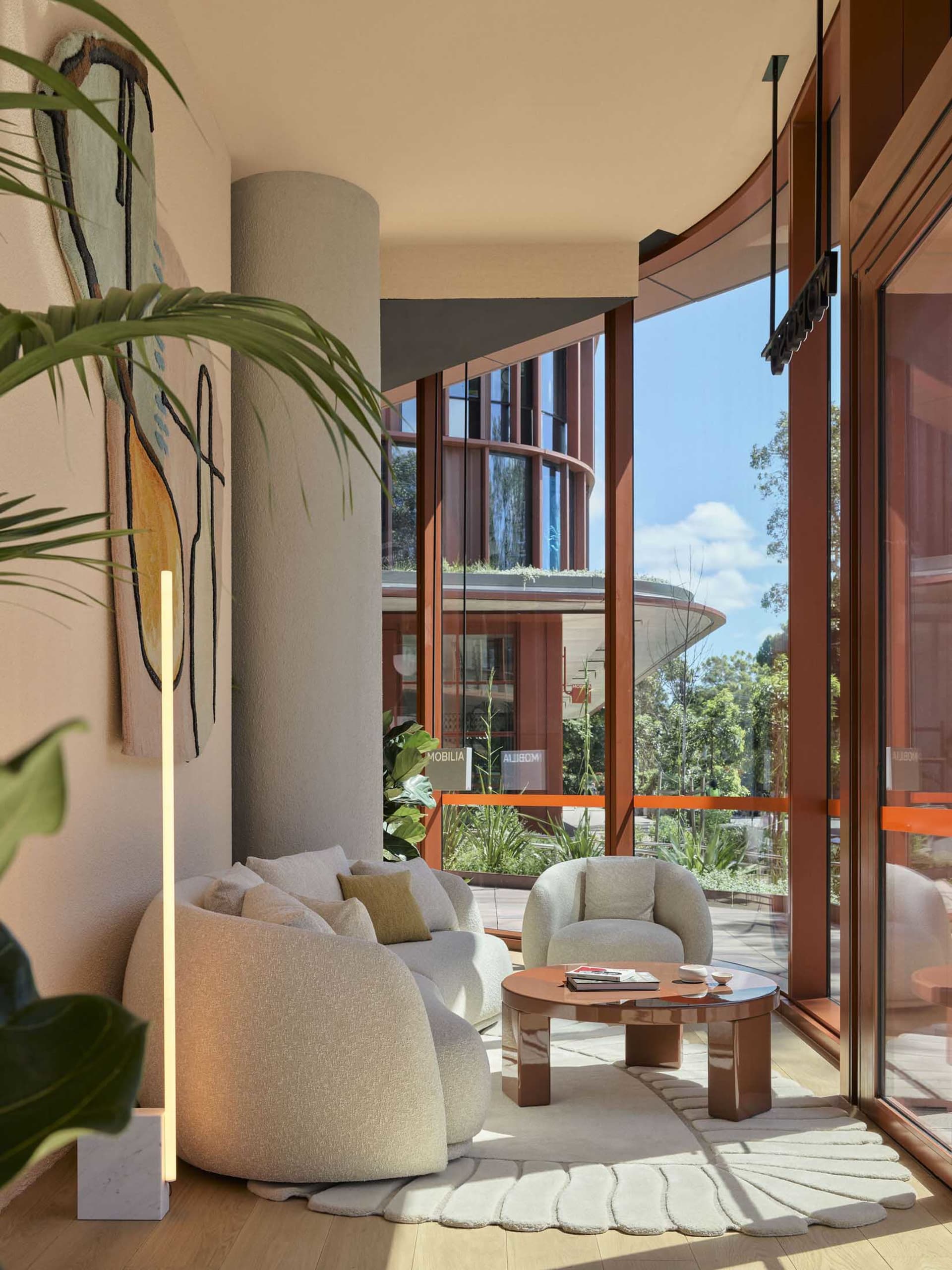 A modern living room with a circular coffee table, plush fabric furniture, and large windows.