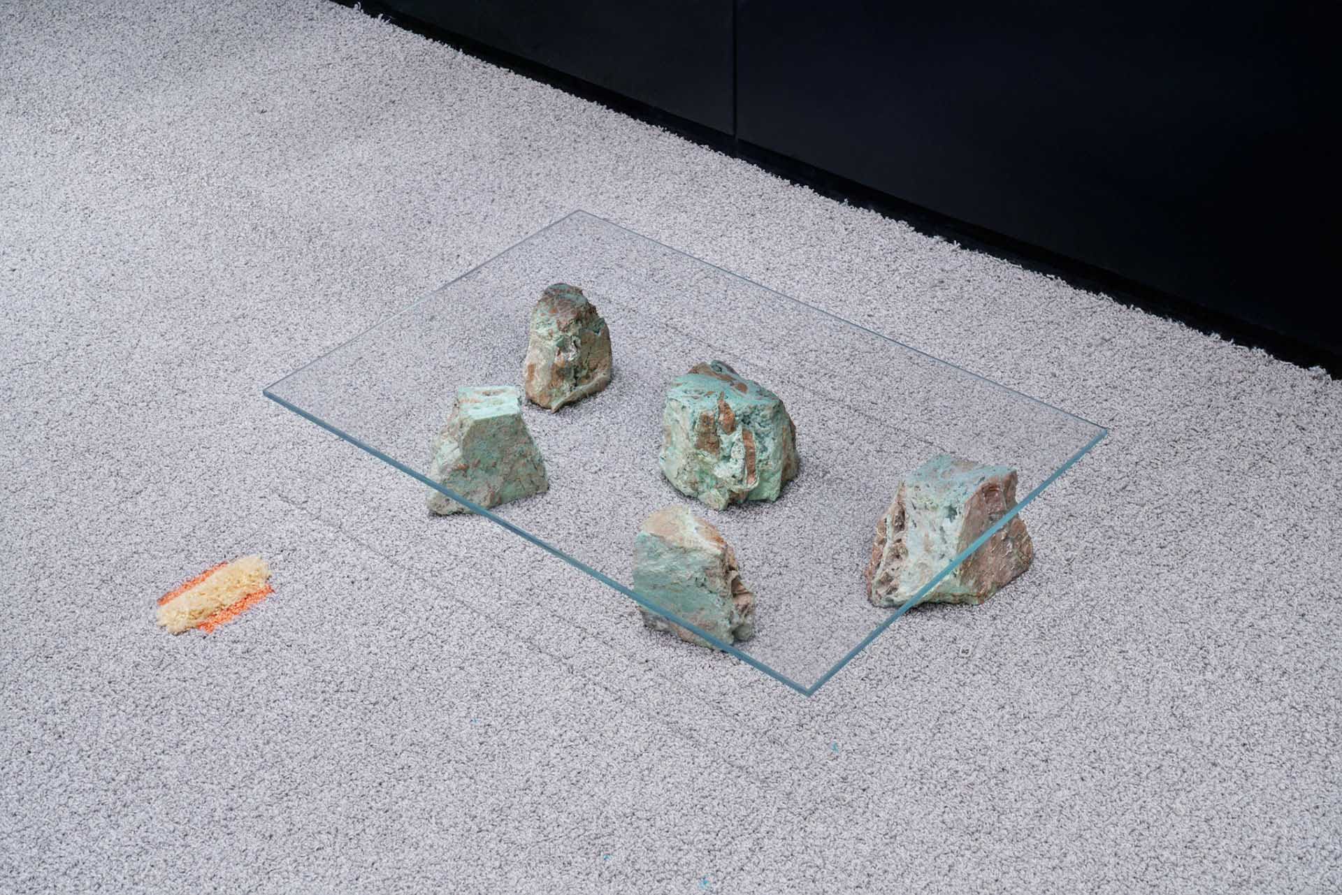 A glass table with green rocks on it, placed on a carpeted floor.