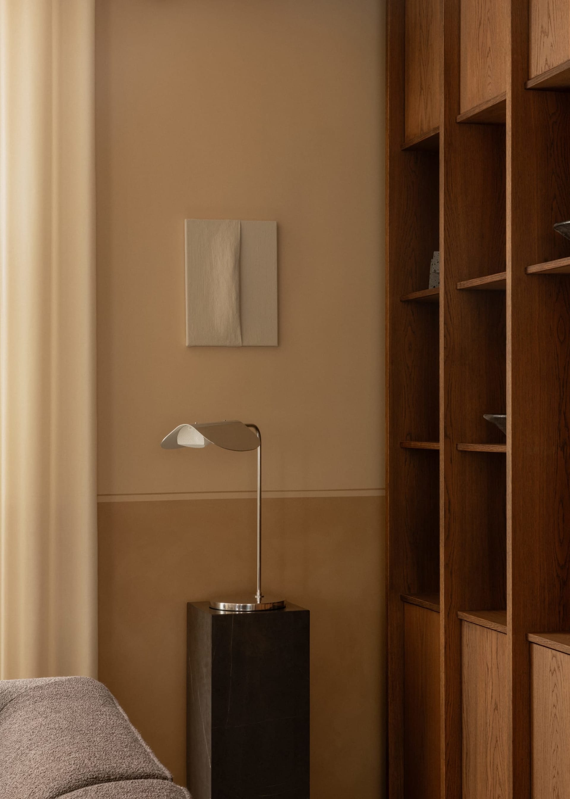 A modern living room with a metallic lamp on a marble pedestal and dark wood bookshelves.