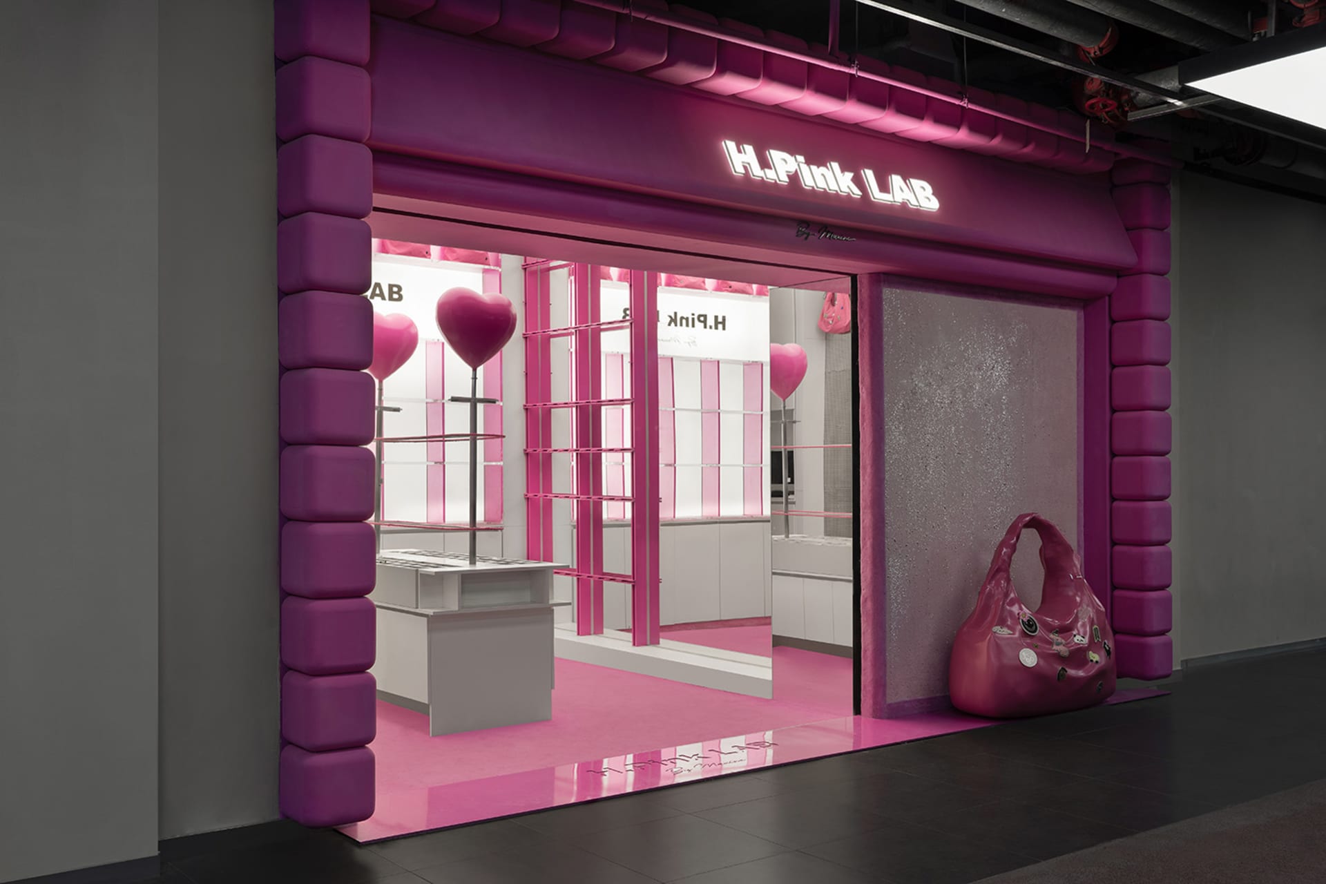 A storefront with pink acrylic elements including a large pink bag, heart-shaped balloons, and a pink floor.