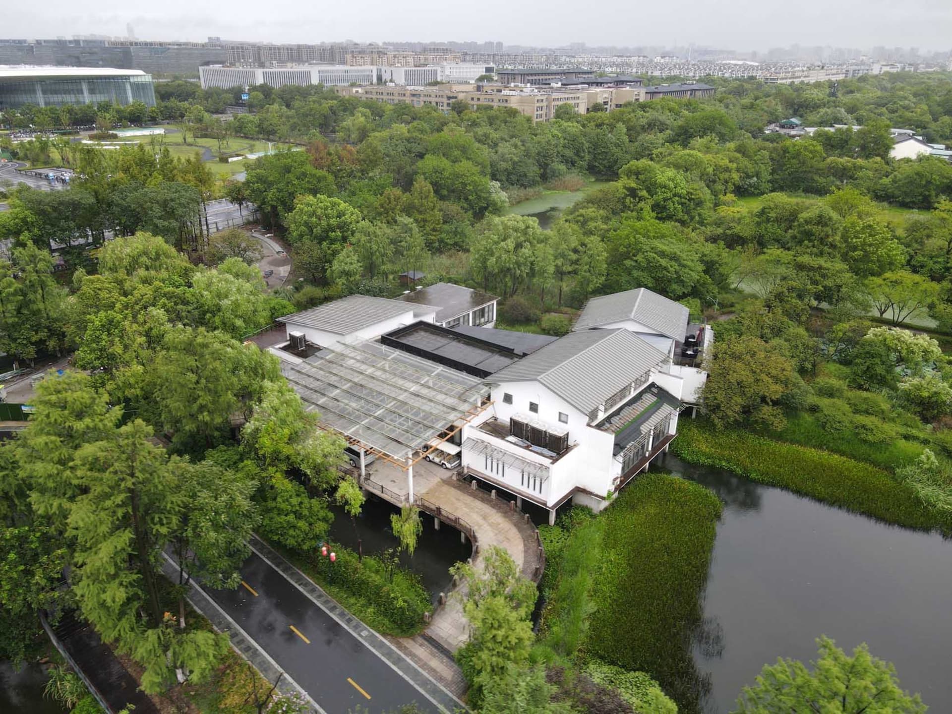 Aerial view of a modern greenhouse structure surrounded by greenery in an urban setting.