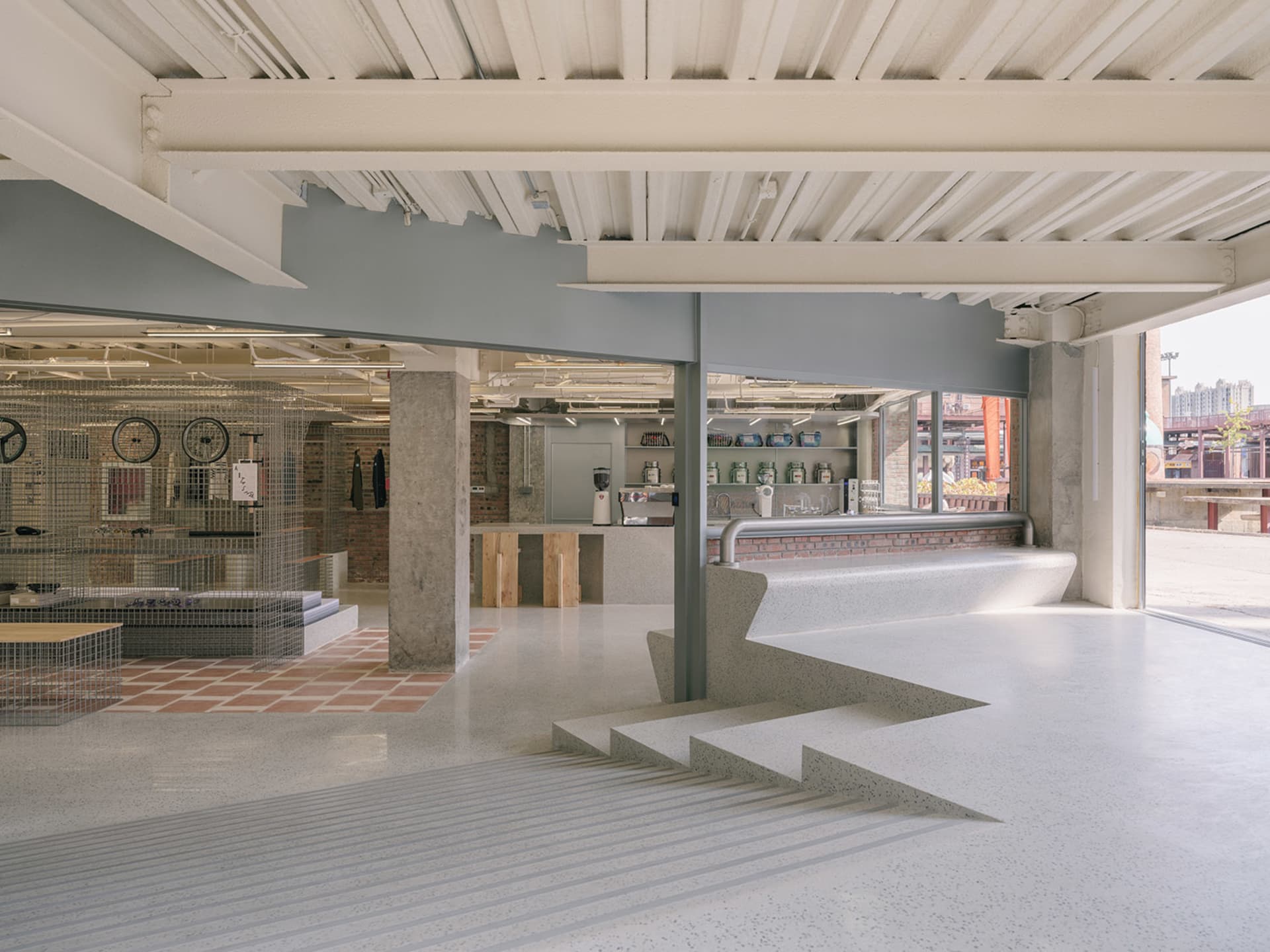 A modern, industrial-style coffee shop with concrete and terrazzo flooring.