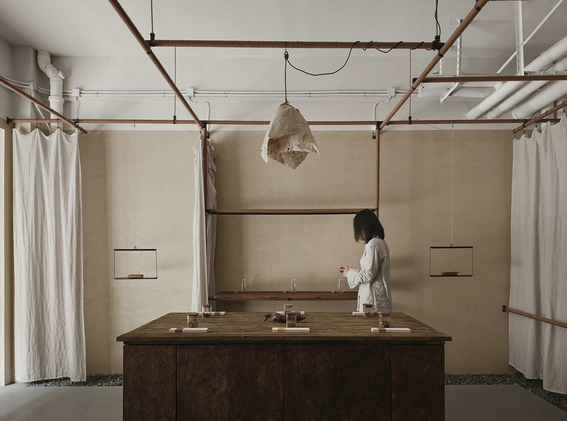 A workspace featuring a wooden counter with various objects and a person standing behind it, surrounded by hanging fabric cur