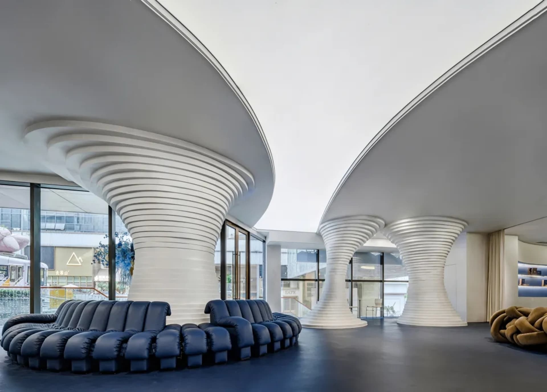 A modern retail storefront featuring curved white structures and a blue sofa in the foreground.