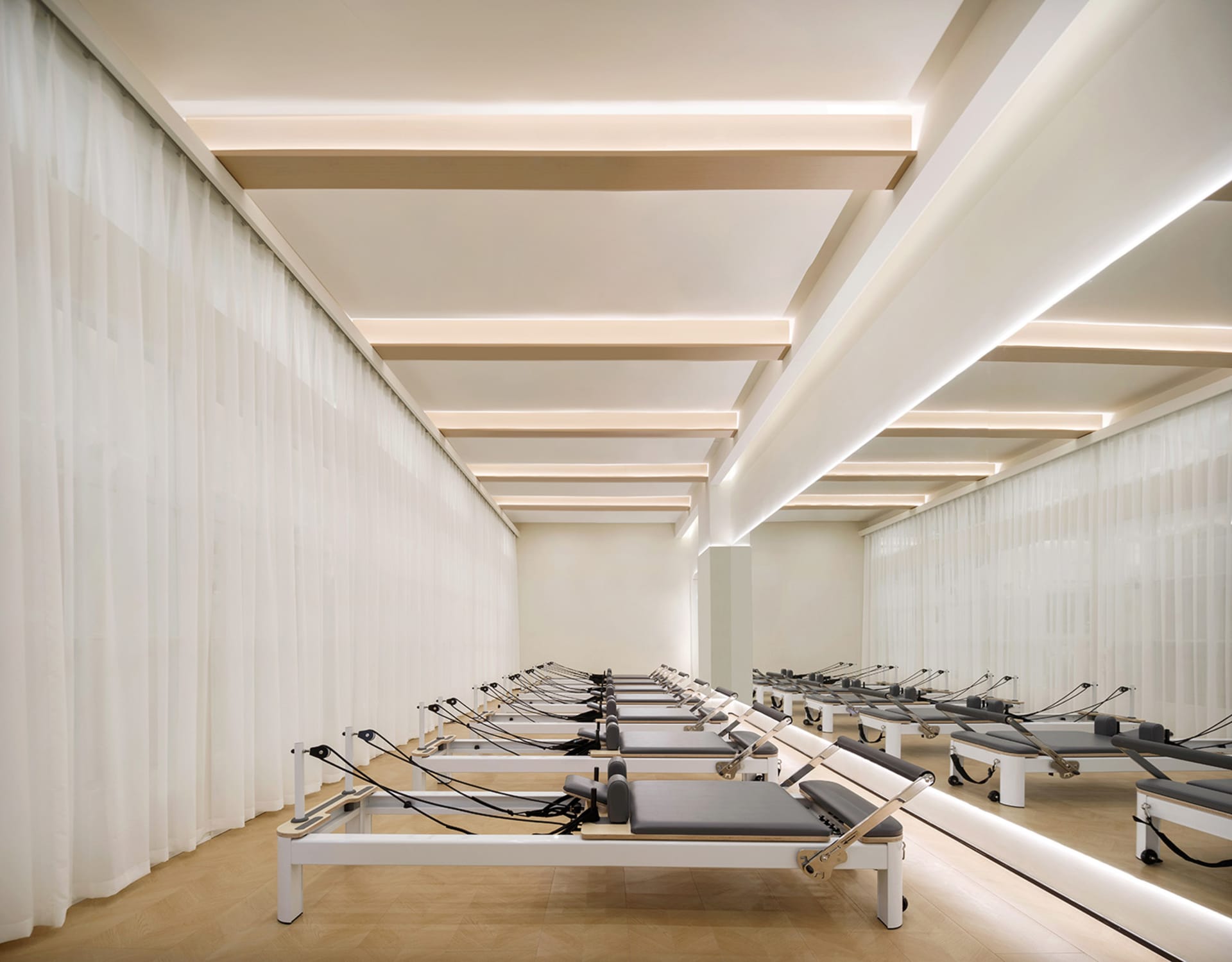 A minimalist fitness center with curtained walls and Pilates reformers lined up in rows.