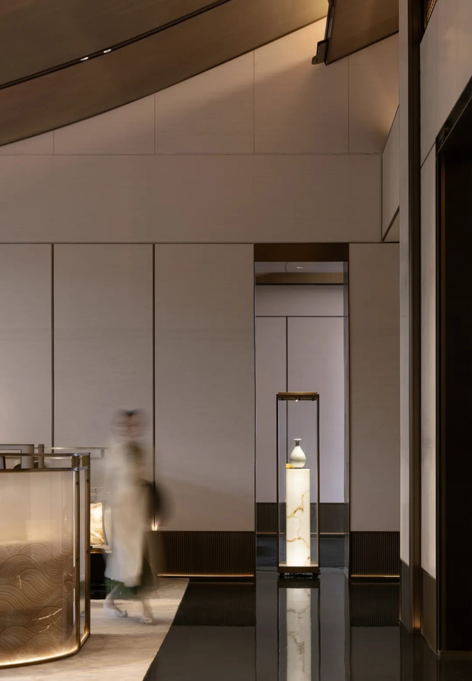 A spacious hotel lobby with sleek, metallic and glass design elements, illuminated by warm lighting.