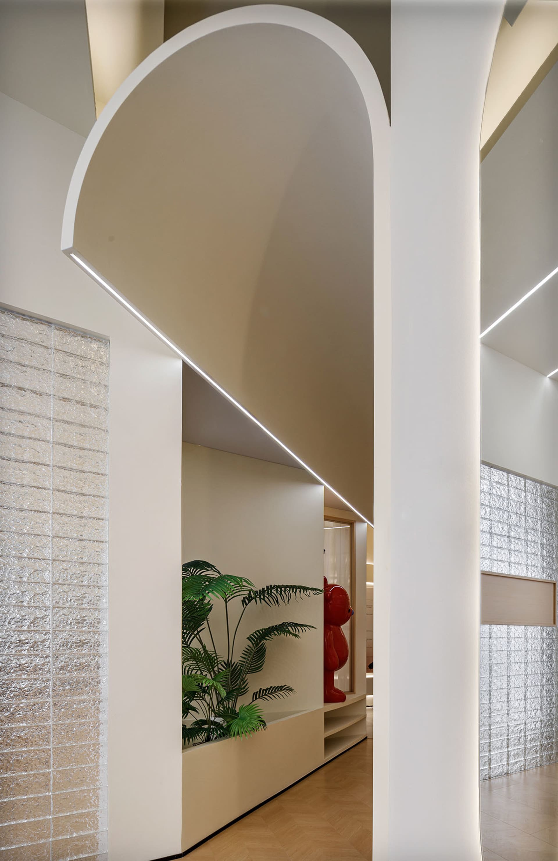 A modern hallway with white concrete walls, textured brick columns, and a lush green plant.