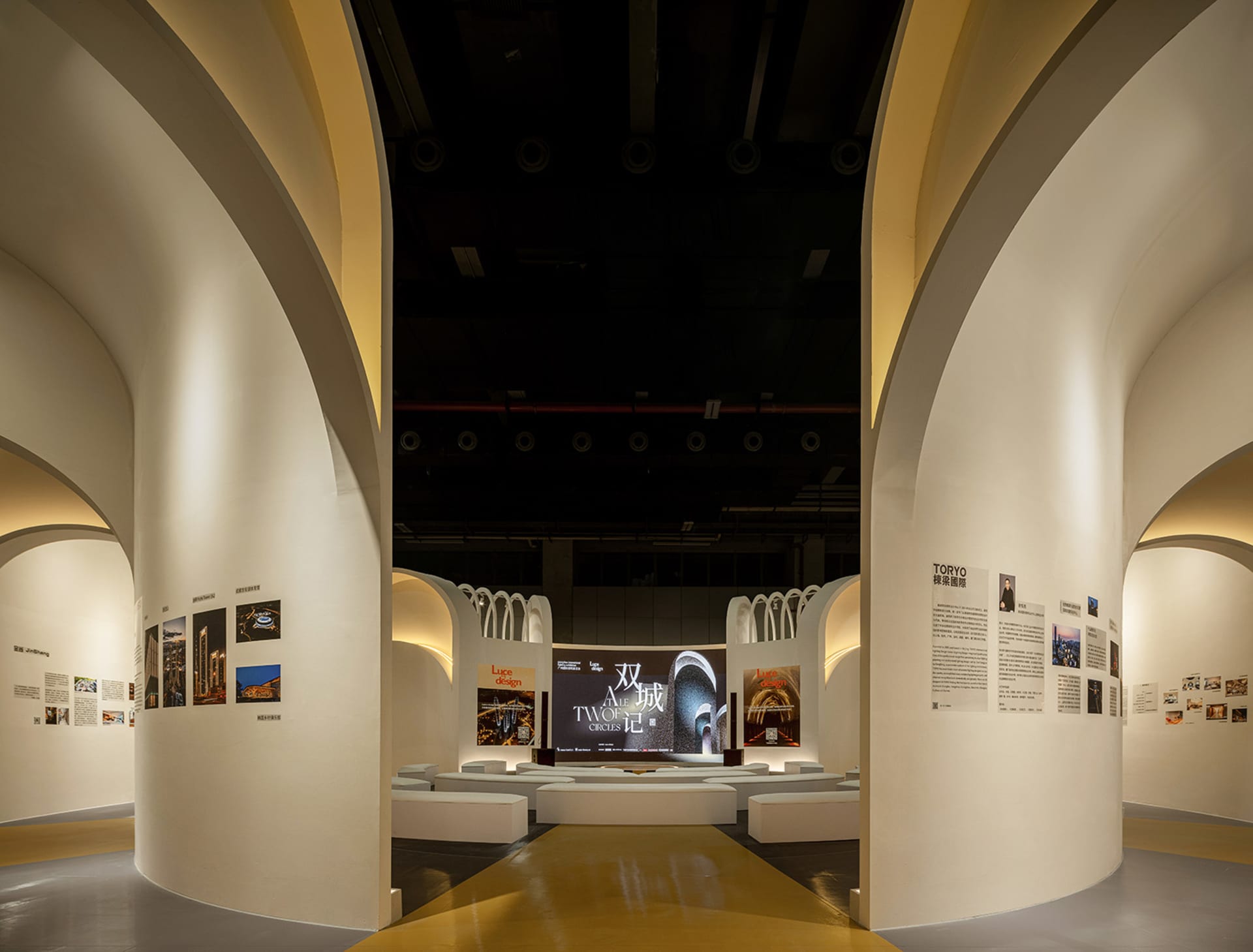 Modern exhibition space with gold accents, featuring a curved wall with artwork and a central display area.