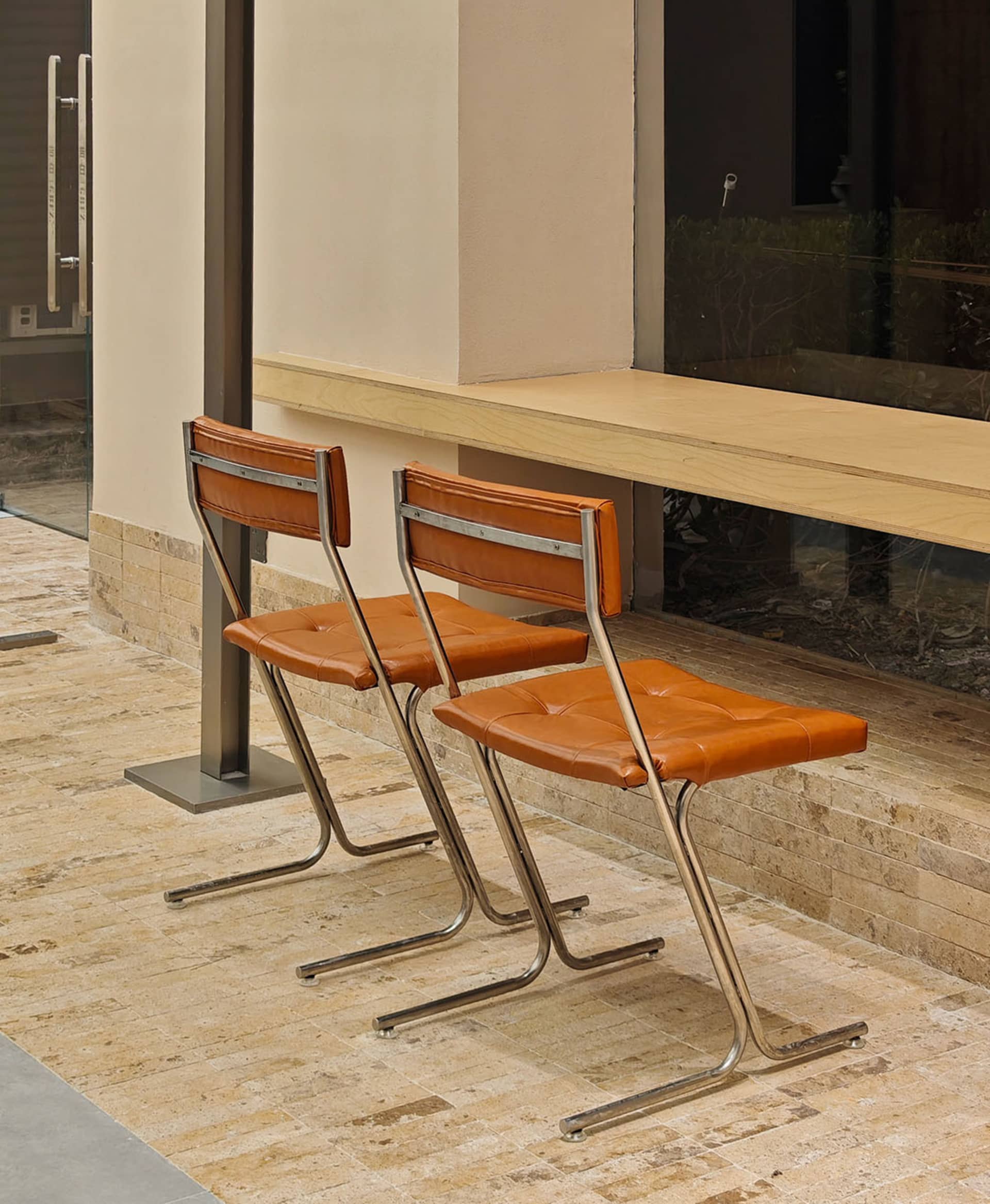Two modern industrial chairs with copper-colored leather seats and backs, set against a neutral-colored wall and floor with a