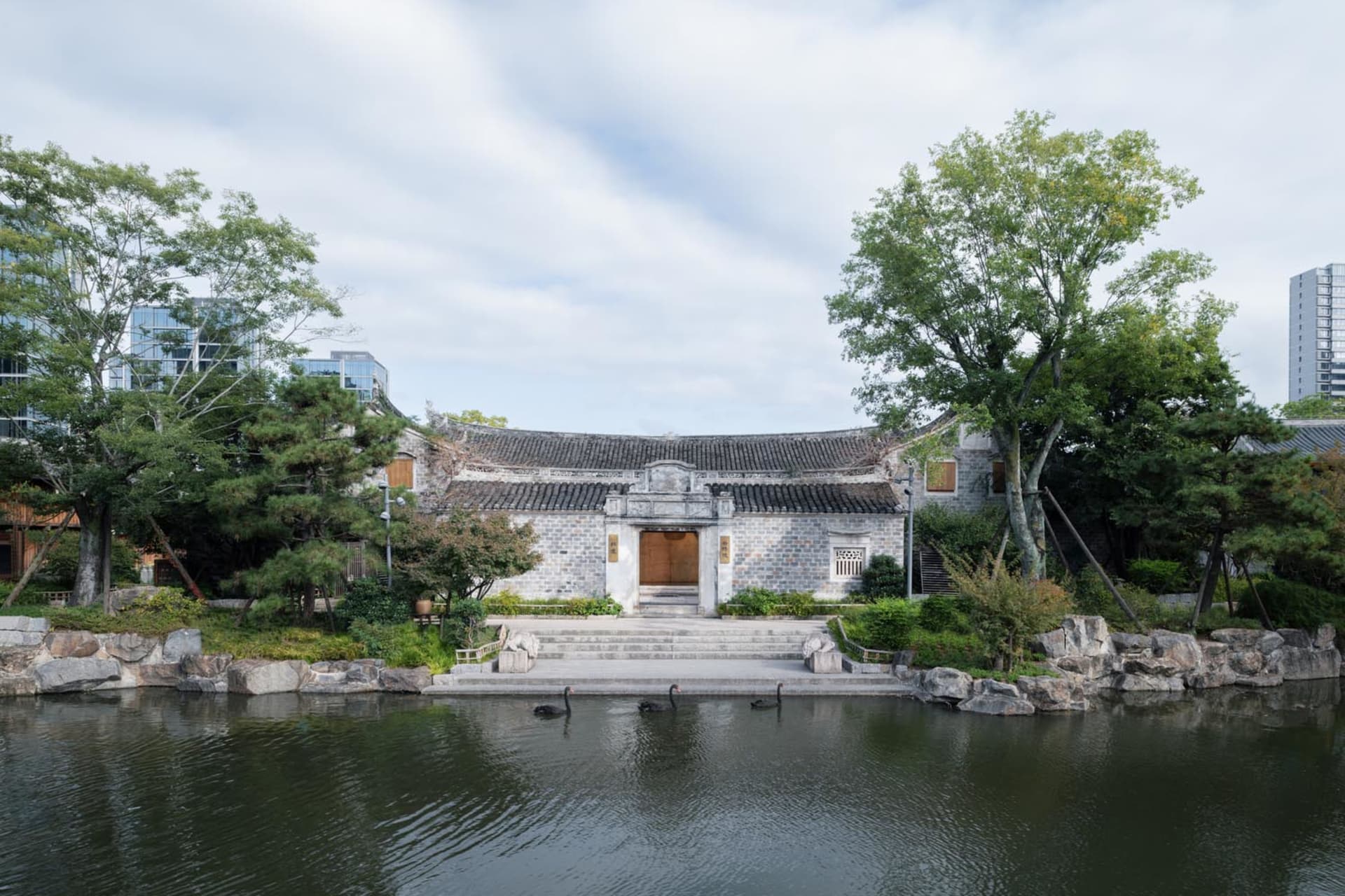 傳統中式建築被石牆環繞,湖面有樹木與黑天鵝