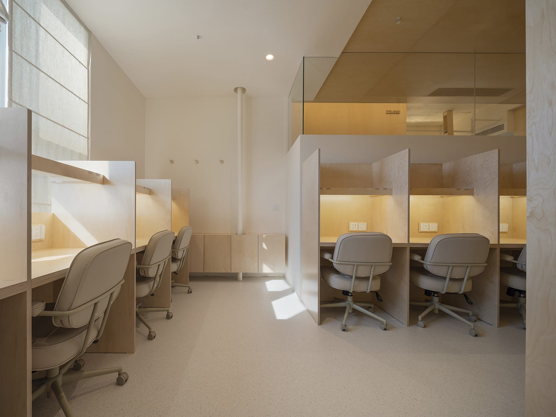 Minimalist private study cubicles with beige chairs and wood paneling.